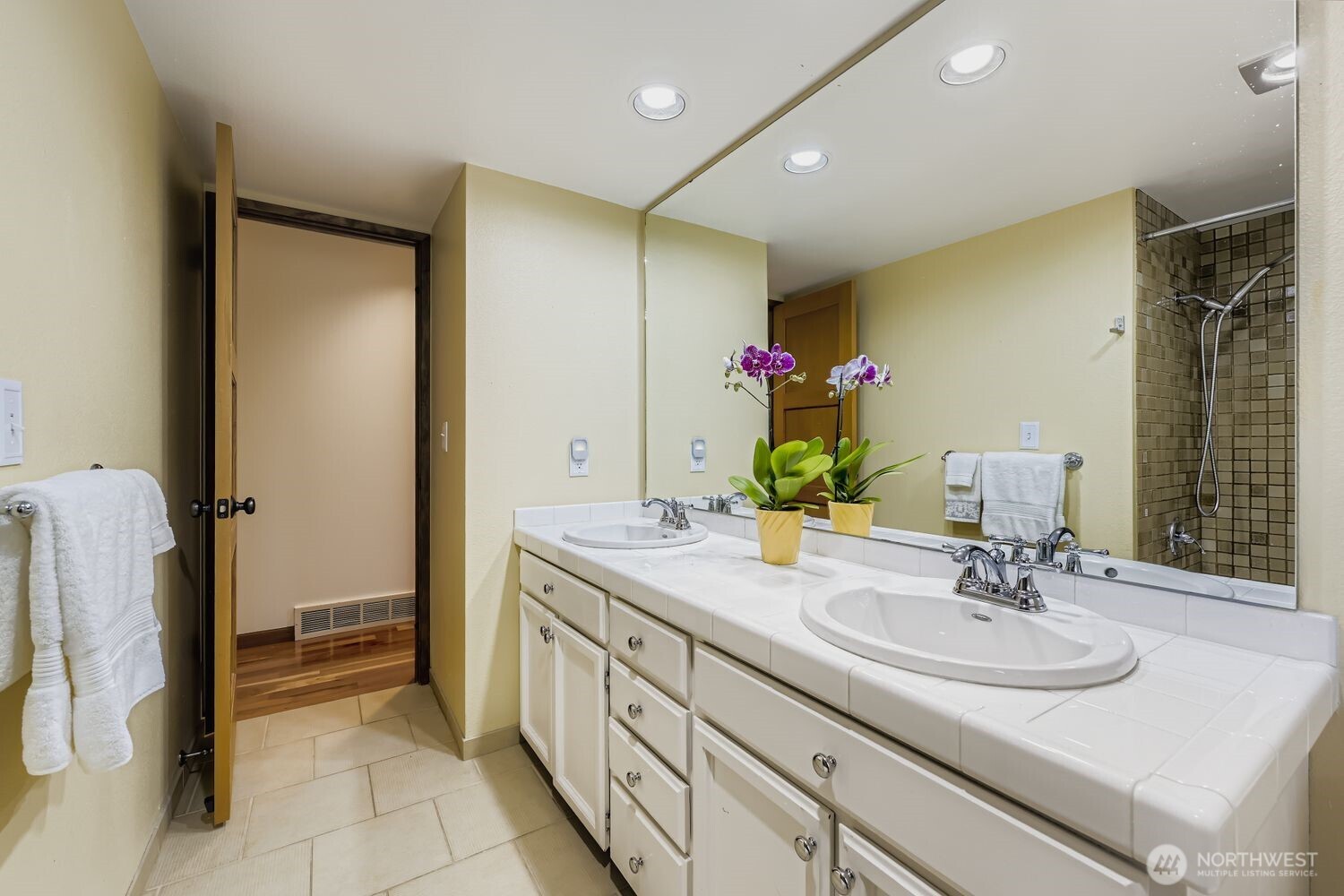 The full guest bath features dual sinks, tile countertops and many drawers and cabinets in the vanity.