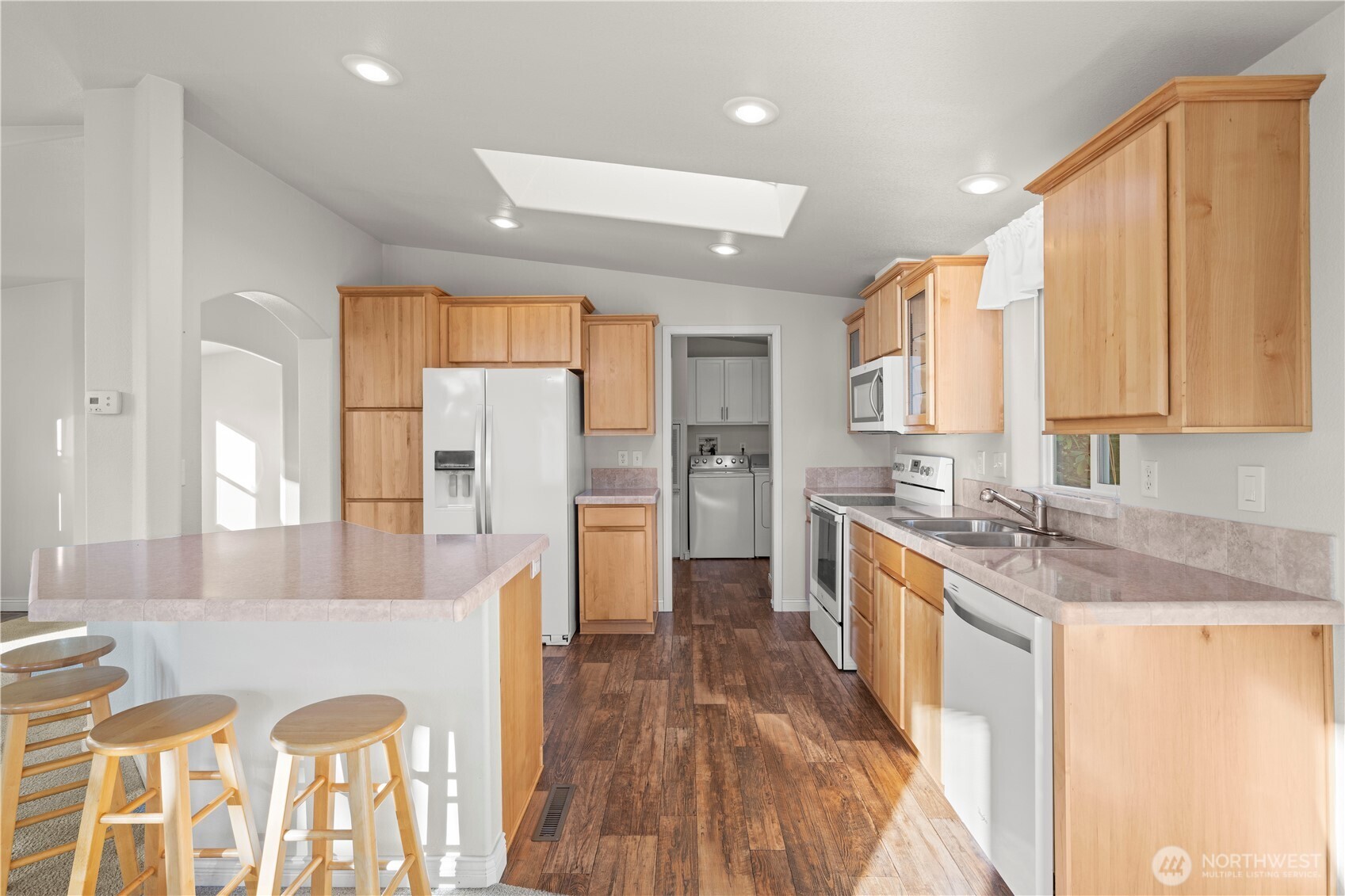 Step into this bright and inviting kitchen, featuring natural wood cabinetry, ample counter space, and a skylight that fills the room with warm, natural light. Equipped with matching Whirlpool appliances, including a microwave, oven, and dishwasher, this space combines functionality.