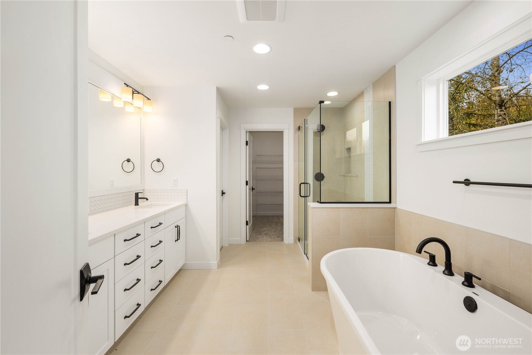 This beautifully designed bathroom features a freestanding soaking tub, dual vanities with abundant storage, and a large glass-enclosed shower. Warm tile tones and modern black fixtures elevate the space into a calming, spa-like experience.    These photos are from lot 3 at Gooden Hollow, the actual home for sale. However, other homes may vary, so all photos, renderings, site maps, and floorplans are for visualization purposes only. Plans, colors, building orientation, finishes, home outlook, and other details can and WILL vary.