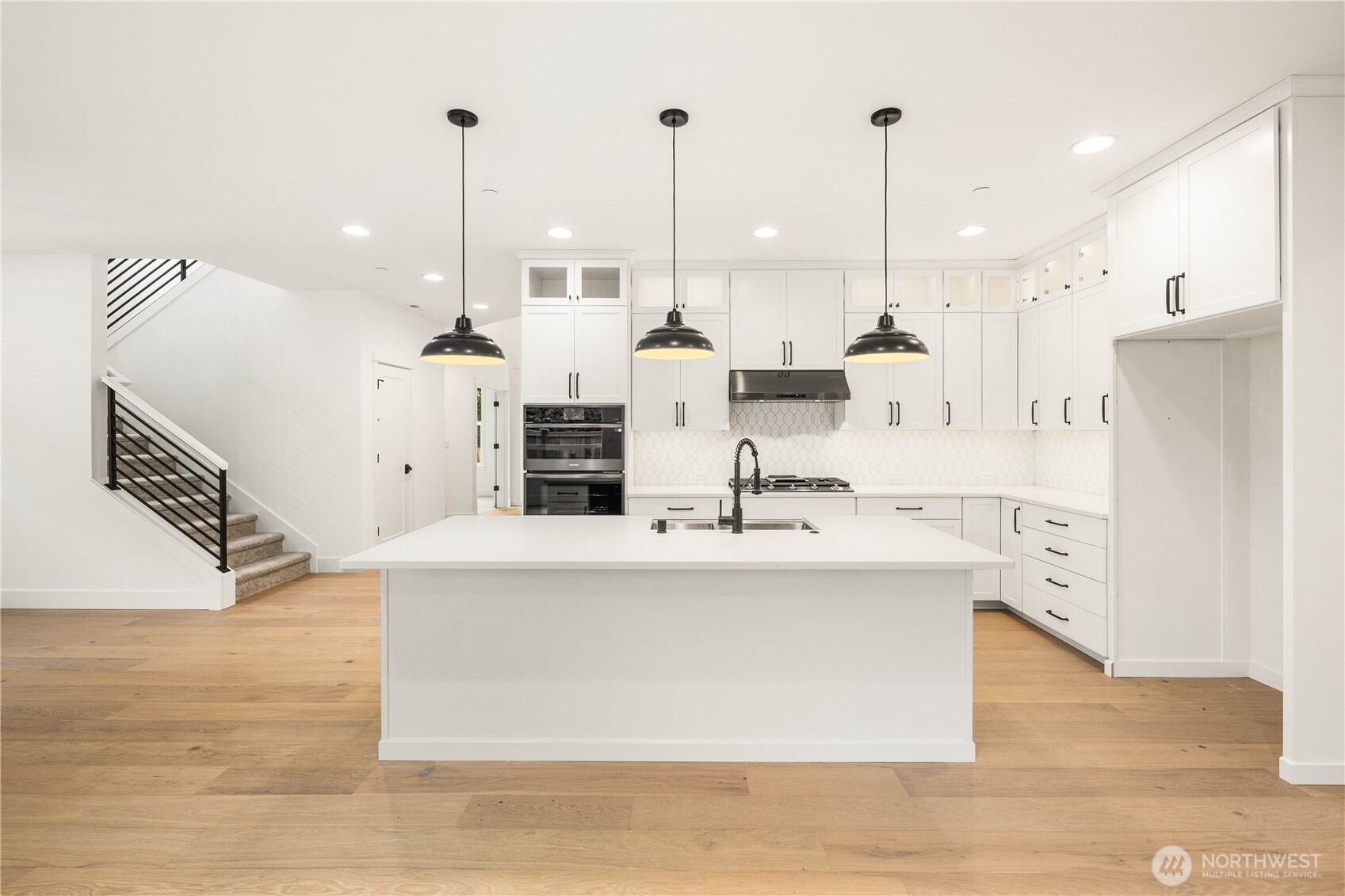 This view showcases the full kitchen layout along with the open railing staircase that enhances the home’s airy, modern feel. The oversized island and extensive cabinetry offer both style and storage, while the open flow supports seamless movement between the main living spaces. It’s a bright, spacious hub designed for modern Eastside living.    These photos are from lot 3 at Gooden Hollow, the actual home for sale. However, other homes may vary, so all photos, renderings, site maps, and floorplans are for visualization purposes only. Plans, colors, building orientation, finishes, home outlook, and other details can and WILL vary.