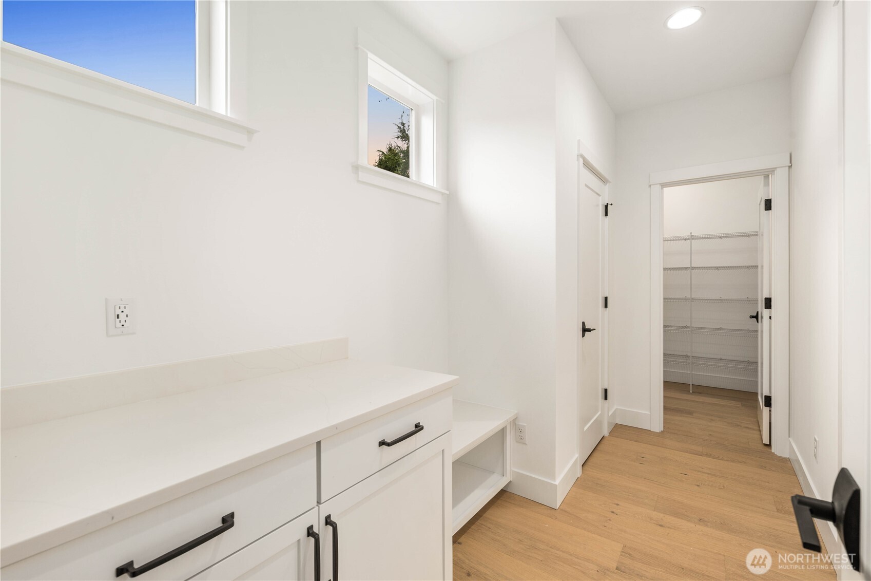 This mud room includes a built-in bench, cabinet storage, and spacious countertop area, offering a practical landing zone off the garage. High windows bring in natural light, keeping the space bright while maintaining privacy. The adjacent walk-in pantry adds extra convenience for unloading groceries and staying organized.    These photos are from lot 3 at Gooden Hollow, the actual home for sale. However, other homes may vary, so all photos, renderings, site maps, and floorplans are for visualization purposes only. Plans, colors, building orientation, finishes, home outlook, and other details can and WILL vary.