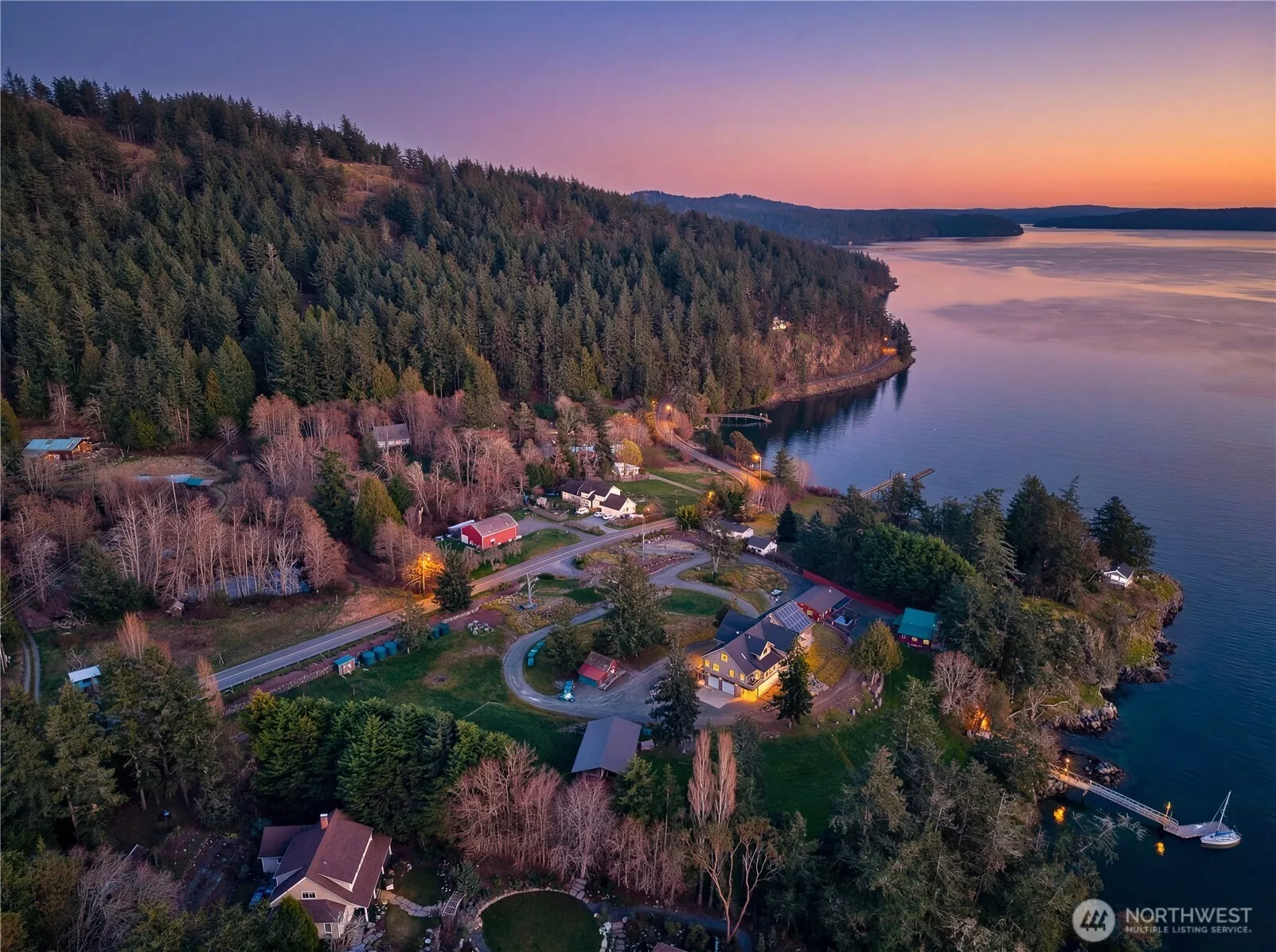 Stunning bird’s-eye view of the property’s waterfront setting at dusk, private deep-water dock, and forested surroundings
