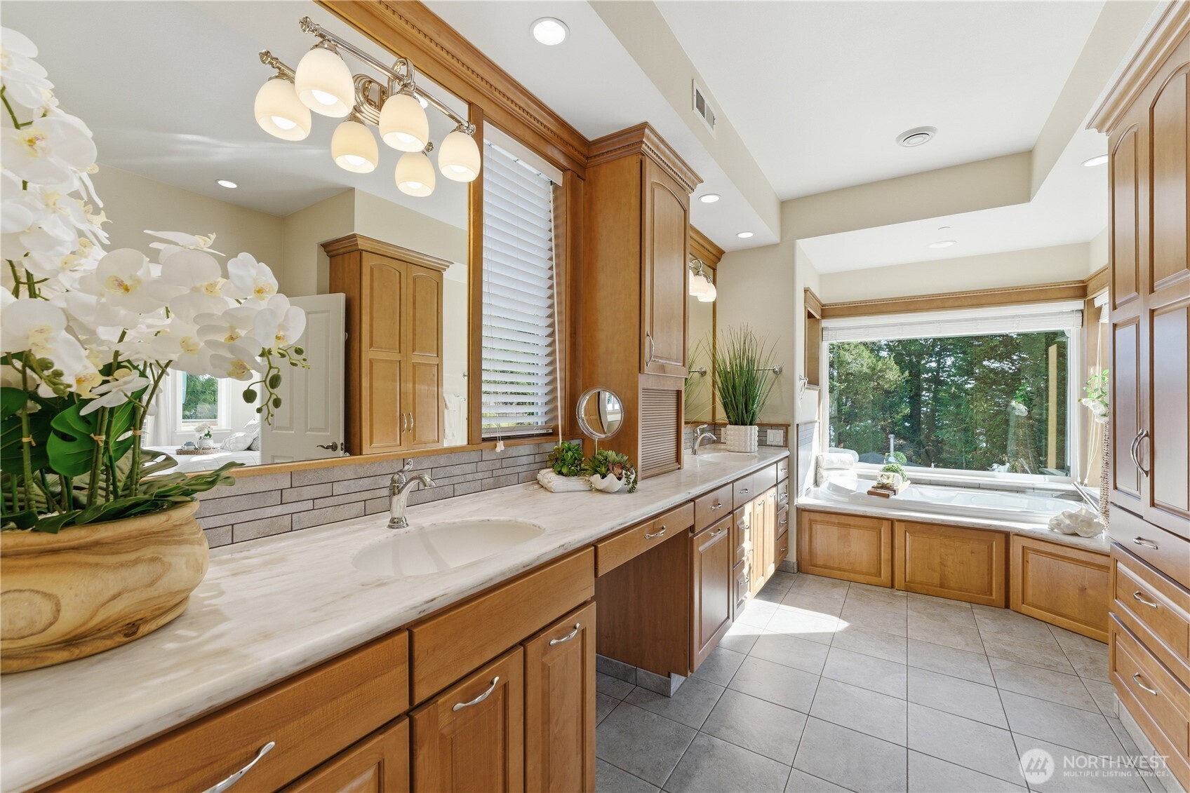 A spacious, light-filled primary bath with double vanities, a deep soaking tub, separate walk-in shower, private toilet and tranquil views - all set within a home warmed by heated floors throughout