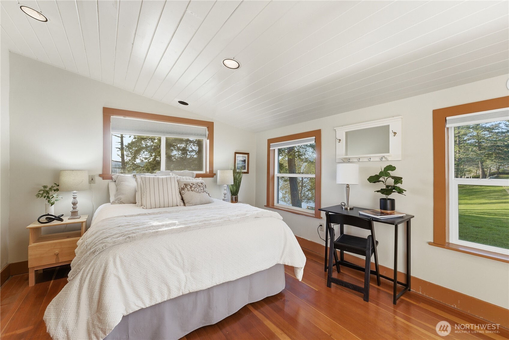 The main bedroom in Cottage #1 offers a bright, inviting retreat with multiple windows framing the surrounding greenery, the sea and natural light