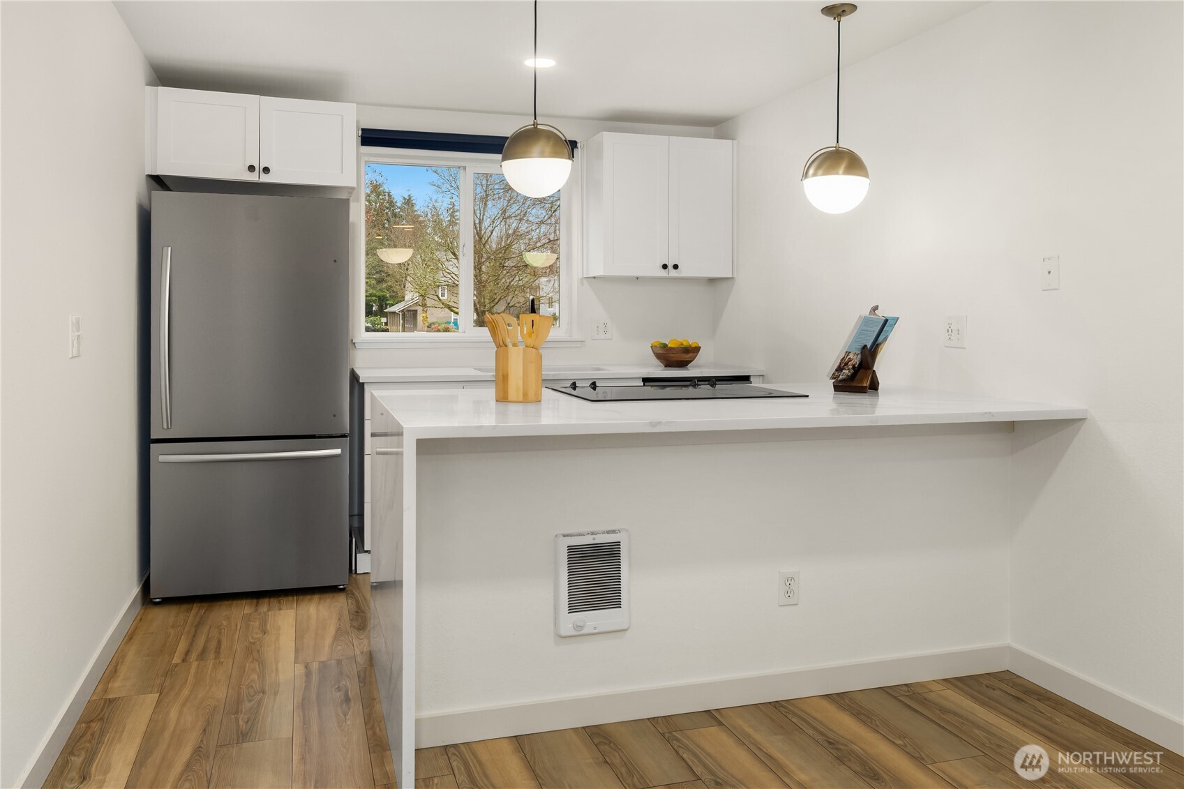 Kitchen with sleek quartz countertops and newer SS appliances. View from bar stool/Dining area on bright kitchen with plenty of daylight streaming in from the kitchen window. What a beautiful view for breakfast!