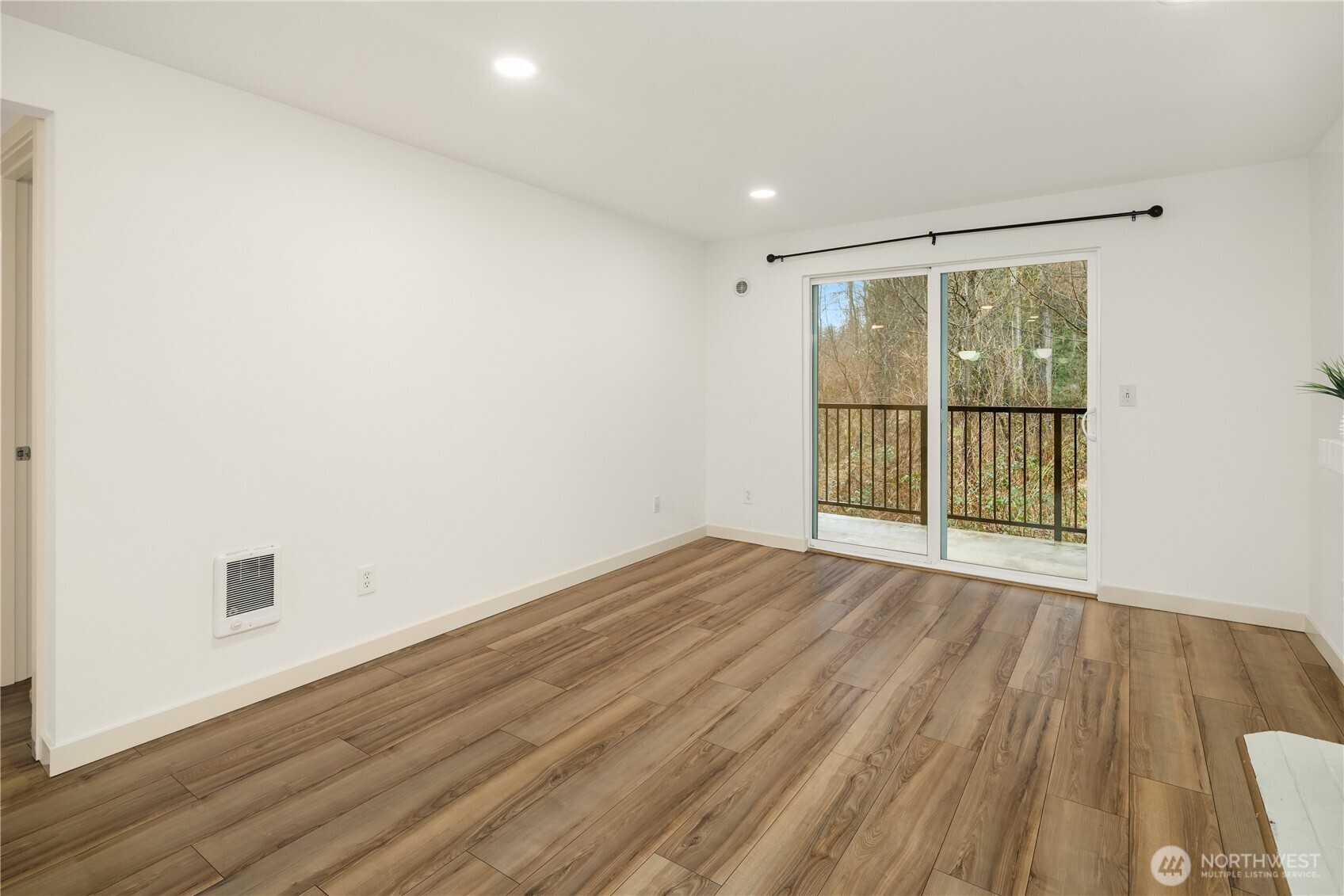 Living area with LVP flooring, TV mount above cozy, wood burning fireplace, and access to balcony with lush greens for peace and quiet.