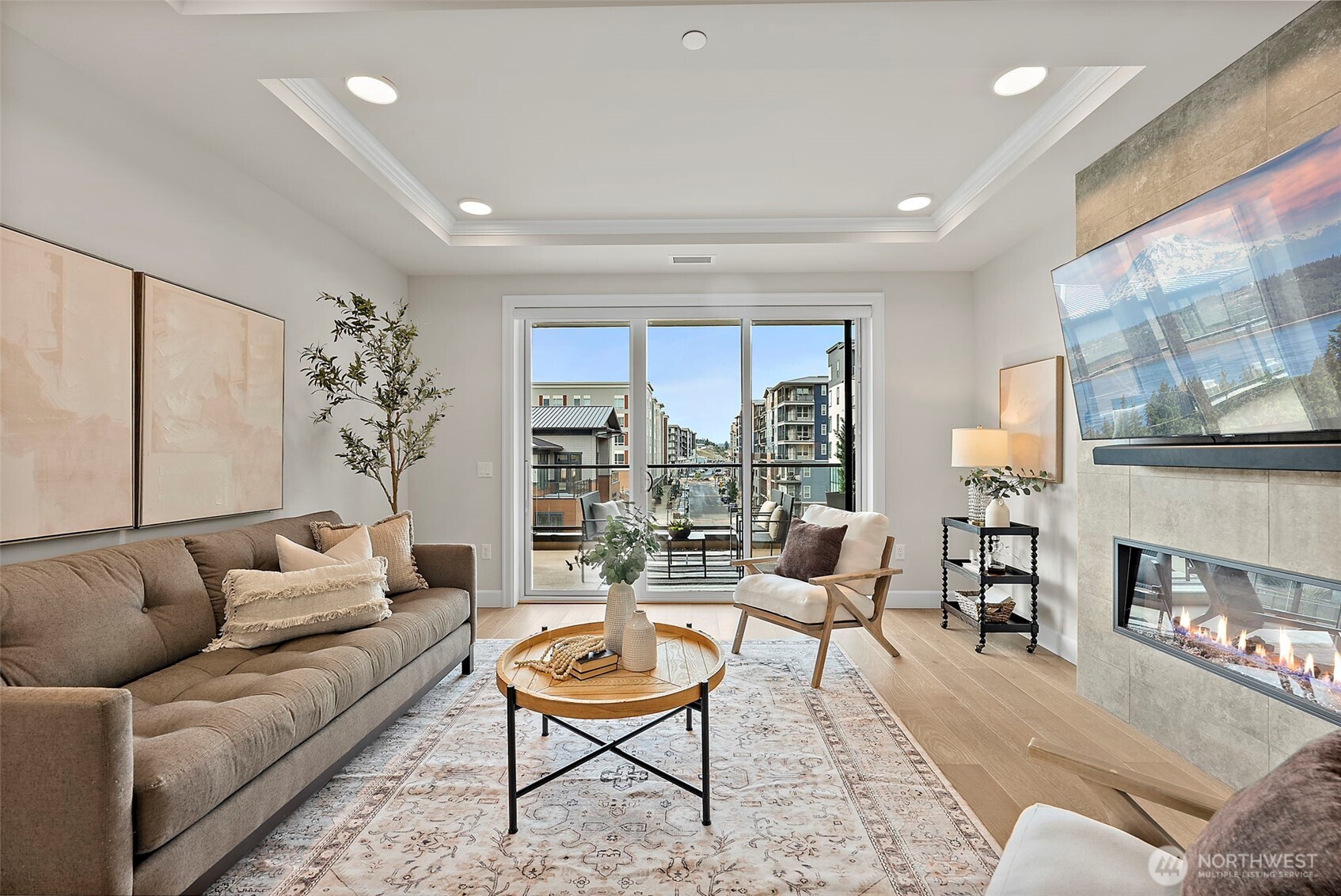 Large glass slider draws in "PNW sunshine" and provides direct access to a private partially covered balcony overlooking the Village at Point Ruston. Cozy stone statement fireplace to the left with attached tv and vinyl plank flooring guiding the flow of the space.