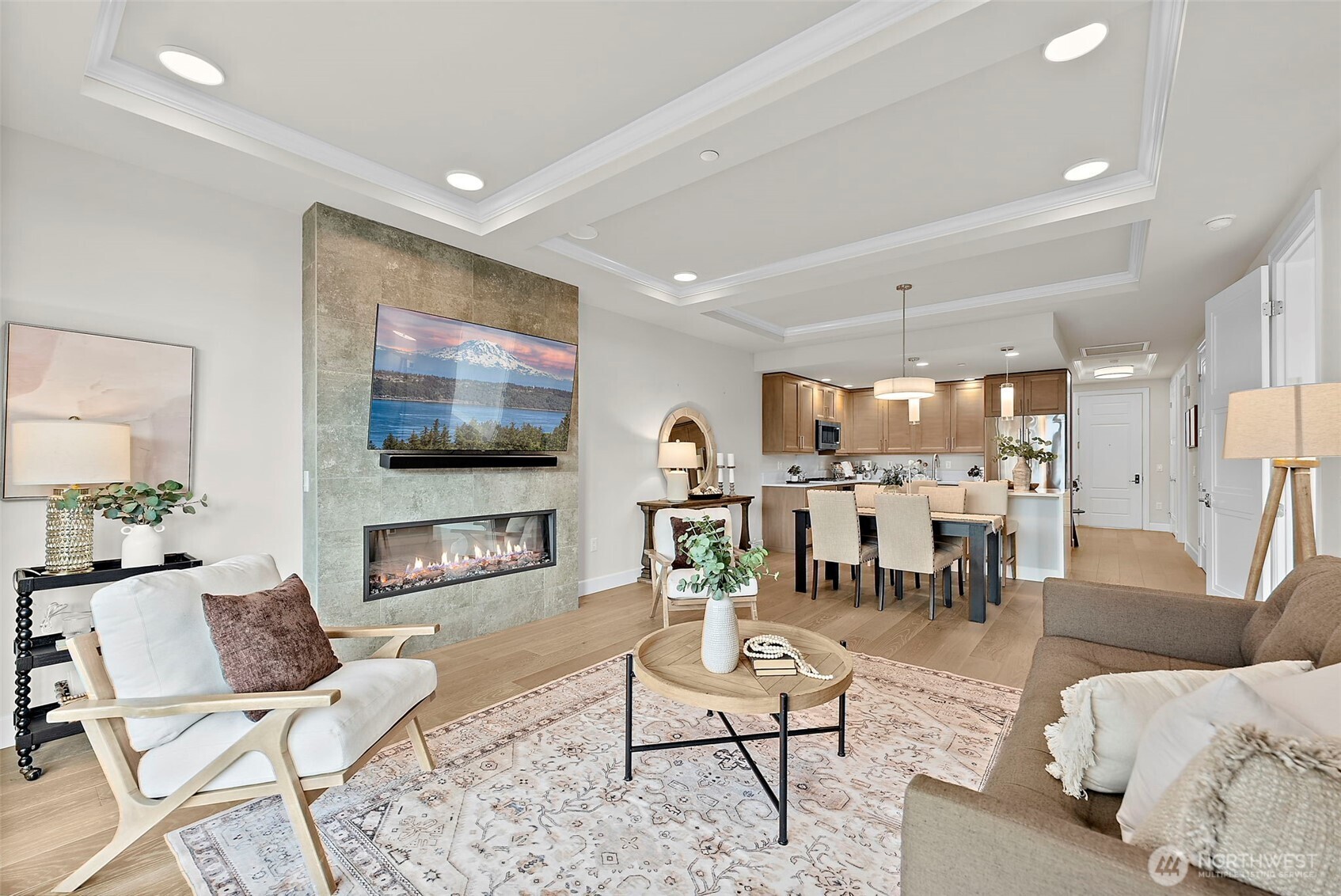 Elevated modern living room with a centerpiece stone floor to ceiling fireplace, vinyl plank flooring, recessed lighting. Open concept layout promotes seamless flow from living to dining to kitchen areas.