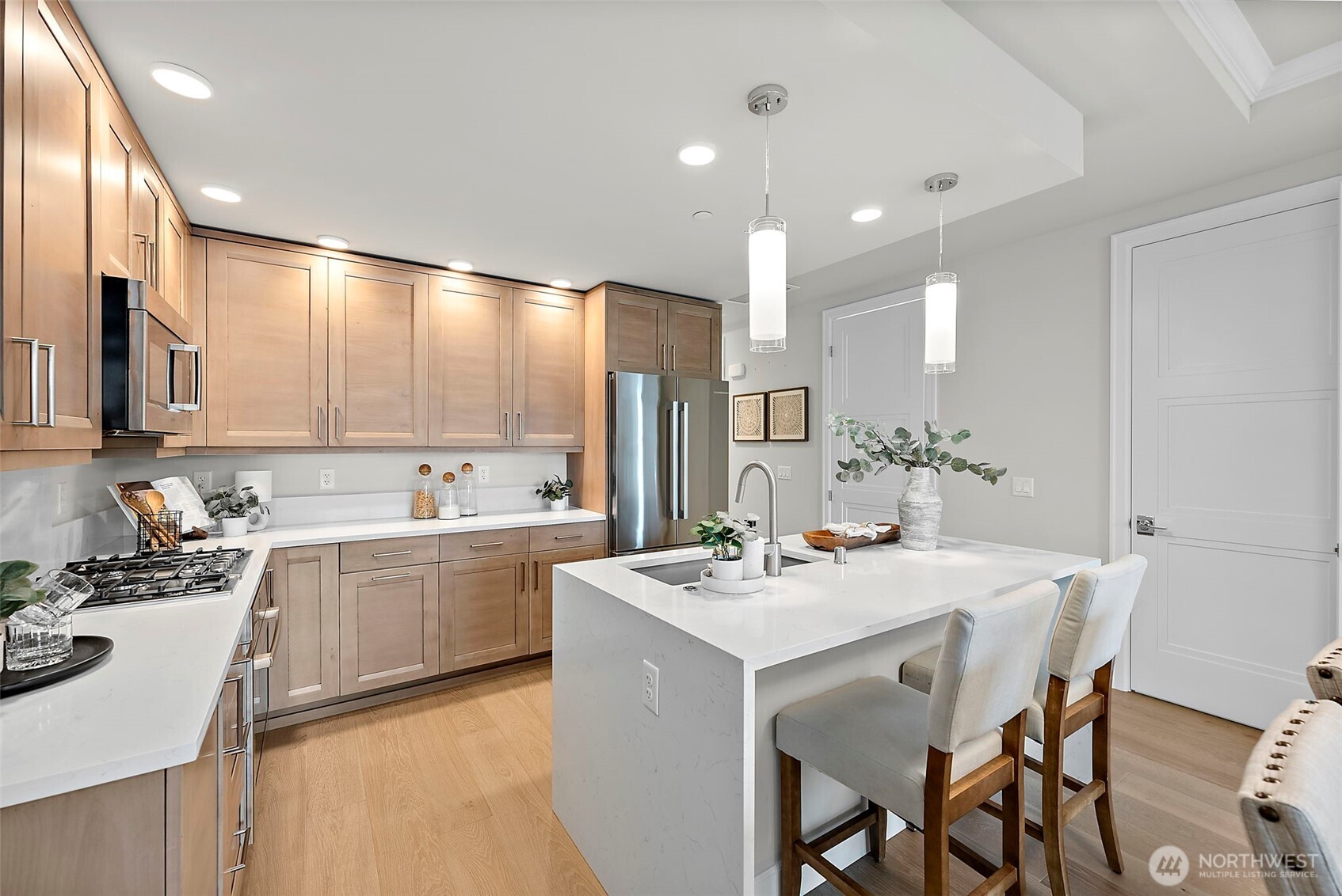 Clean lines and modern neutral tones, with stainless appliances. A central island with space for bar seating, also houses the undermount sink and dishwasher helps maximize counterspace in the rest of the kitchen. Gas cooktop to the left of island. Double-door refrigerator located behdind the kitchen island.
