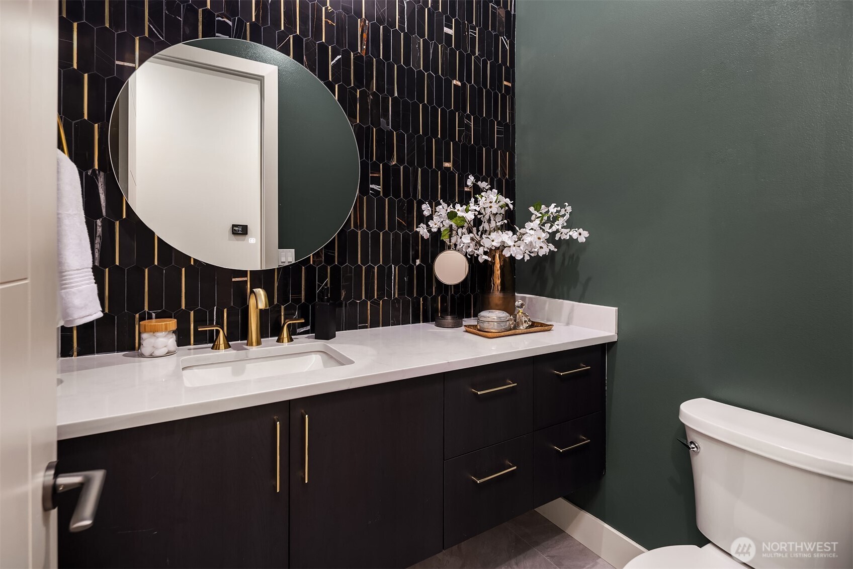 Bold and sophisticated, the main floor powder room features a dramatic tiled accent wall, brass fixtures, and sleek modern cabinetry