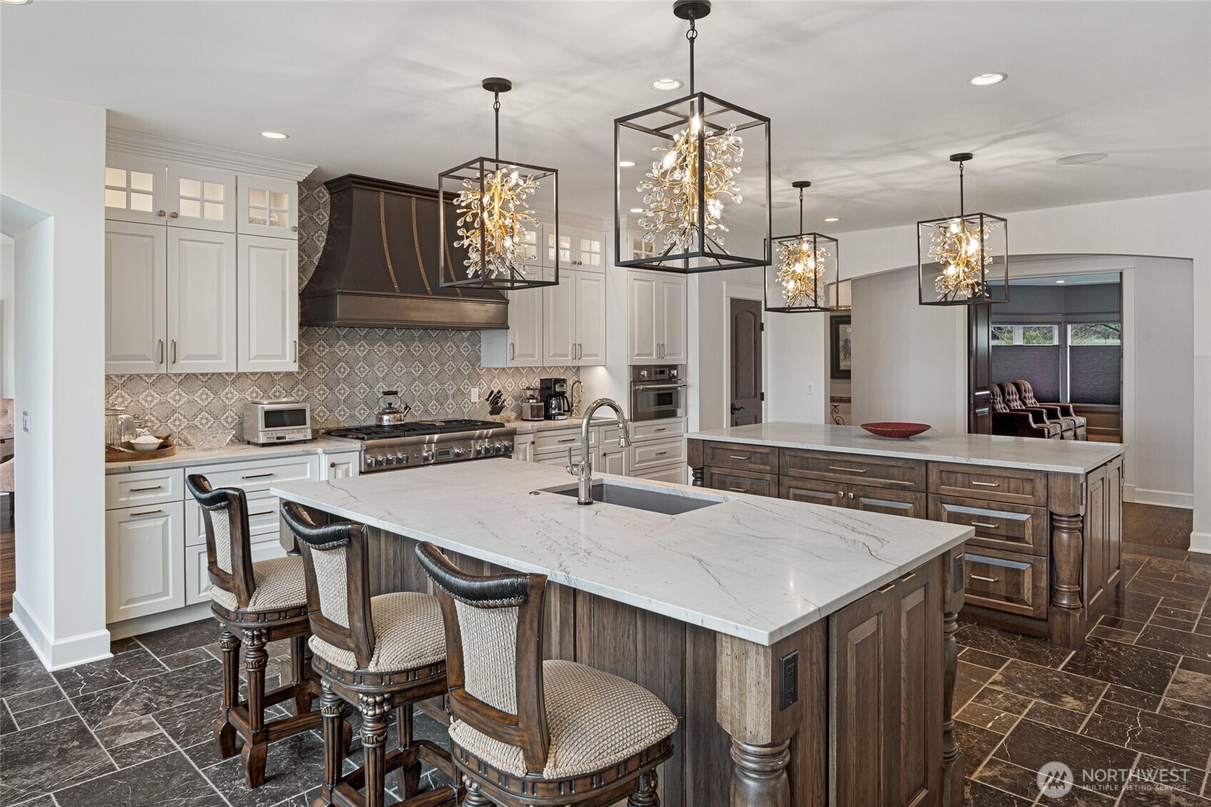 Spacious chef’s kitchen featuring dual oversized islands with marble countertops, custom wood cabinetry, farmhouse sink, and designer pendant lighting.