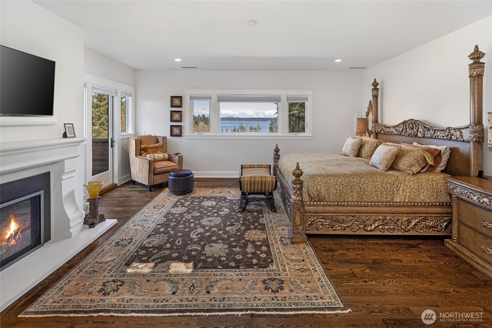Spacious primary suite featuring gas fireplace, hardwood floors, private deck access, and expansive windows capturing panoramic San Juan Channel views.