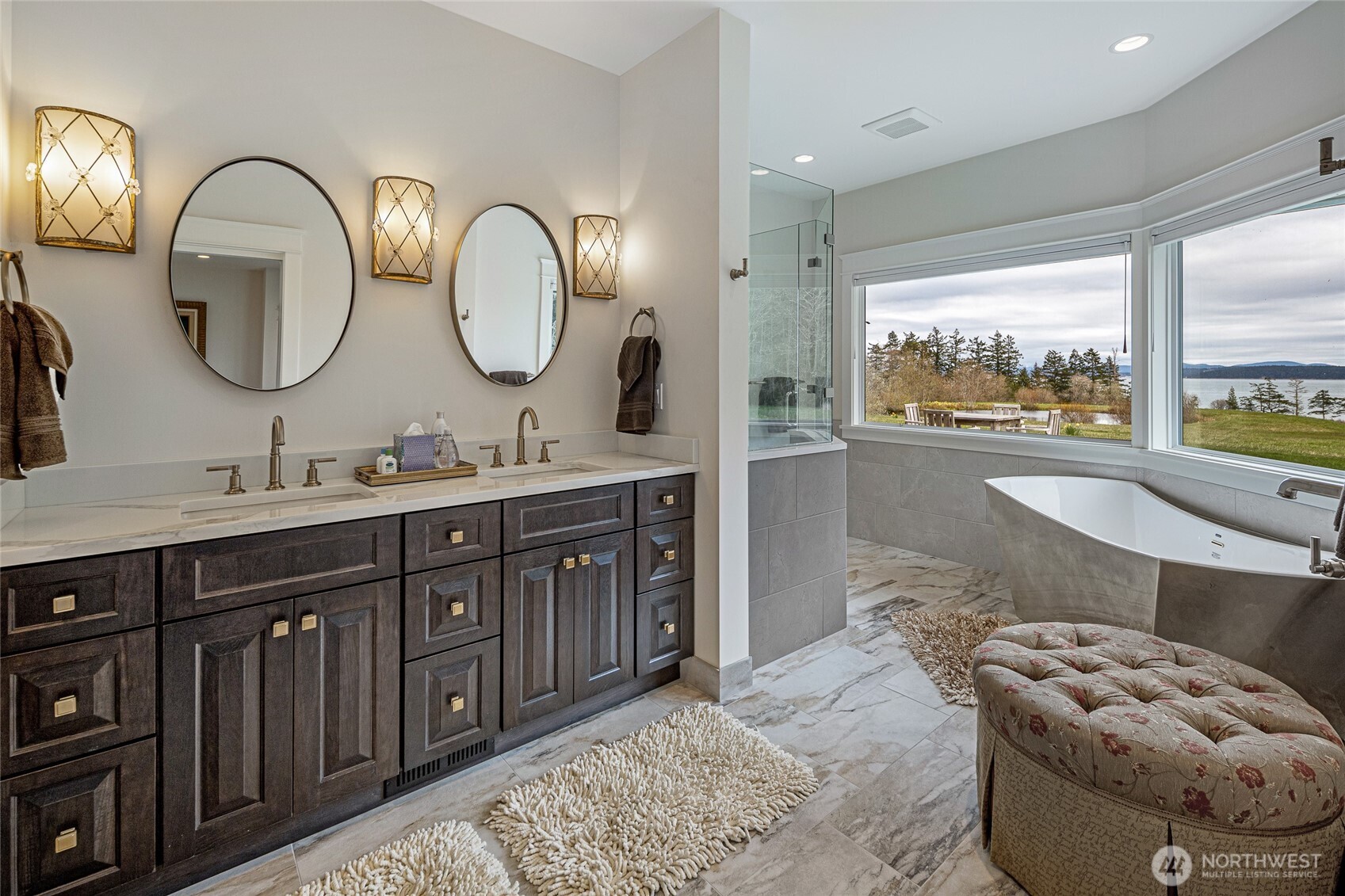 Spa-inspired primary bath with dual vanity, marble tile flooring, freestanding soaking tub, and panoramic water views toward the San Juan Channel.