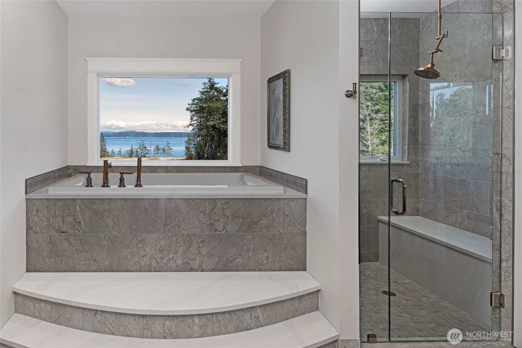 Spa-inspired primary bath with elevated soaking tub framed by picture window, marble tile surround, and sweeping water views toward Mount Baker.