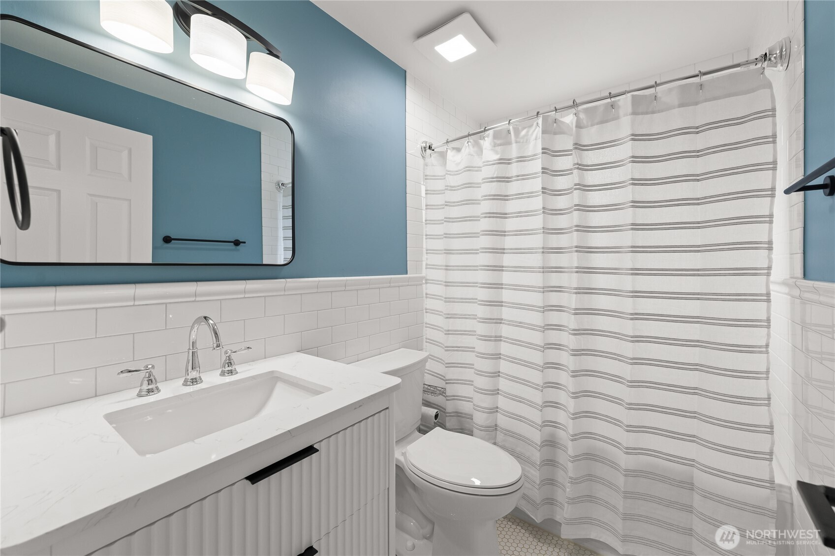 Hallway bathroom featuring a tiled wall and shower, a new 30-inch vanity with ample storage, and updated modern fixtures