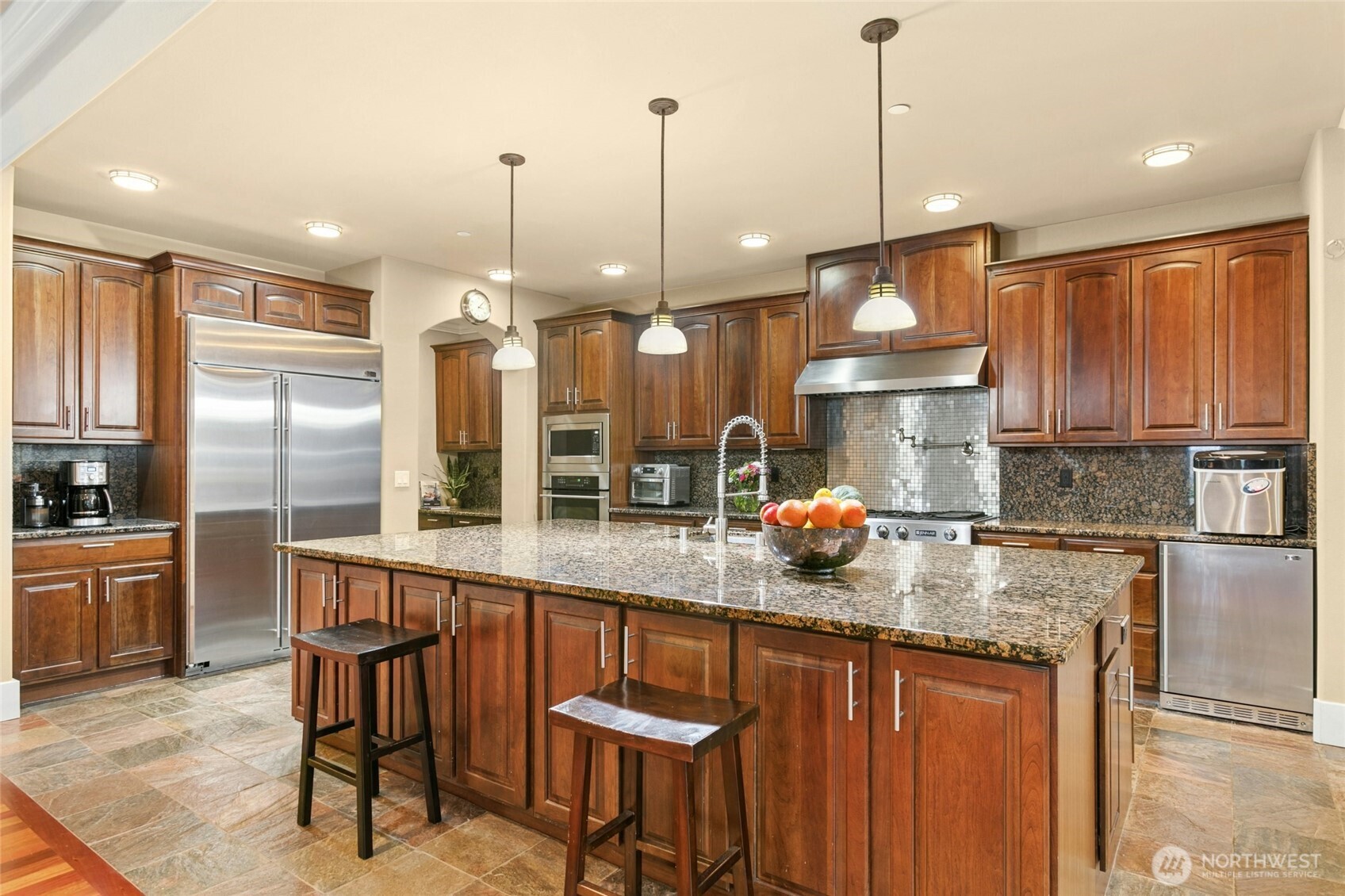 Chef’s kitchen featuring a Jen air 6-burner range with griddle, built-in GE Monogram refrigerator, wall oven and microwave, two Bosch dishwashers, beverage refrigerator, pot filler, and a built-in desk area.