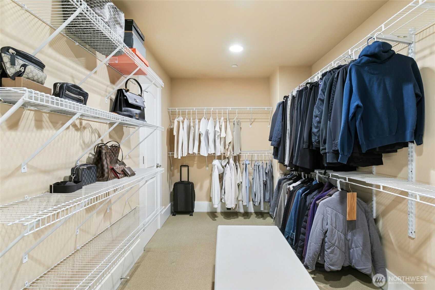 Grand walk-in closet complete with a center bench and an additional dedicated shelving section, thoughtfully designed for maximum organization.