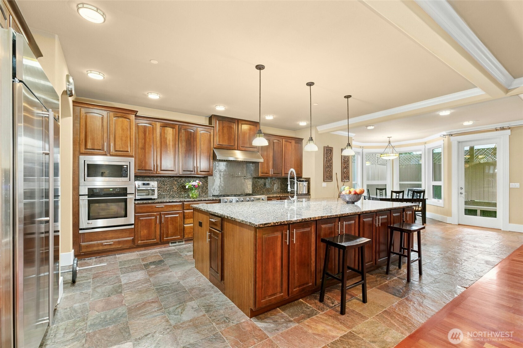 Chef’s kitchen featuring a Jen air 6-burner range with griddle, built-in GE Monogram refrigerator, wall oven and microwave, two Bosch dishwashers, beverage refrigerator, pot filler, and a built-in desk area.