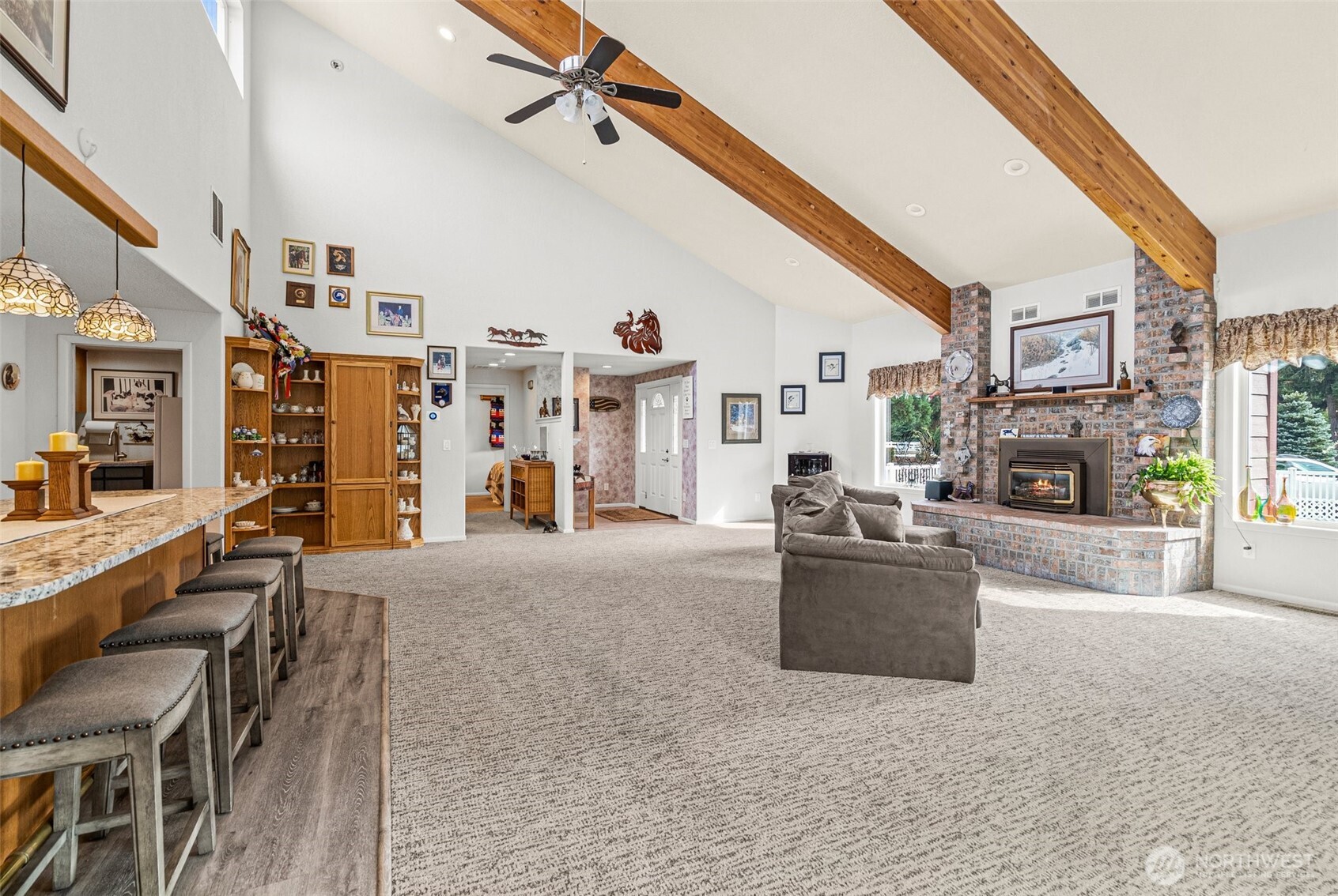 Step into a spacious great room with soaring vaulted ceilings, accented by rich wood beams, and abundant natural light, the Clerestory windows bathe the room in sunlight. At the heart of the room, a classic floor-to-ceiling brick fireplace adds warmth and timeless charm.
