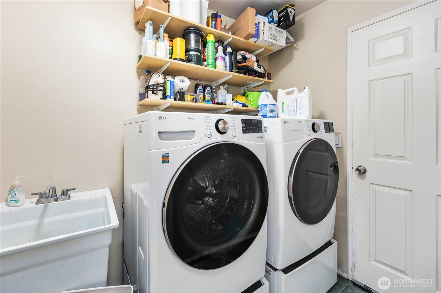 Functional laundry suite featuring high-efficiency machines, a utility sink, and convenient overhead storage.