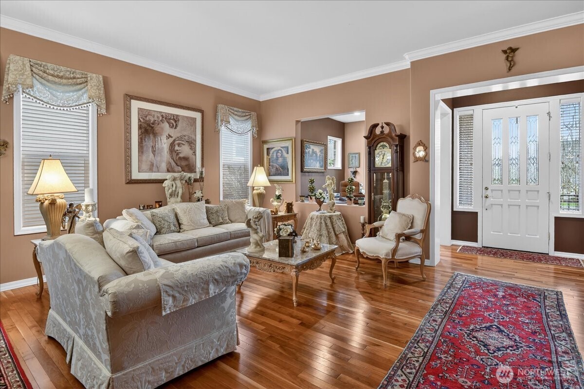 This Grand Living and Dining space is adorned with Crown Moldings, wrapped windows, elegant window treatments, a gas fireplace, classic Chandelier, and warm, custom paint.