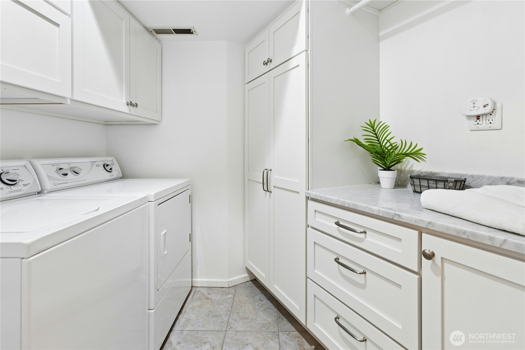 Lower level laundry room with tile floors, Speed Queen washer and dryer, plenty of cabinets and hanging space.