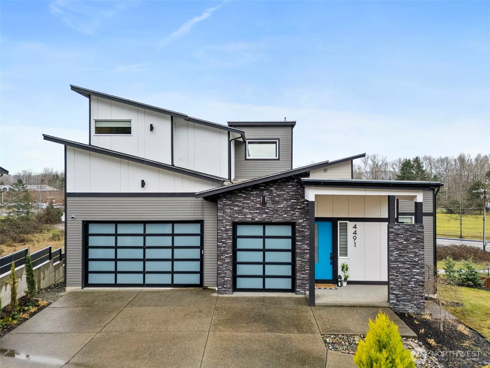 Modern exterior of a contemporary home for sale in the River Rock subdivision, featuring clean architectural lines, stone accents, a spacious driveway, and attached garage. Aerial and front views highlight its setting within the scenic River Rock community surrounded by natural greenery.