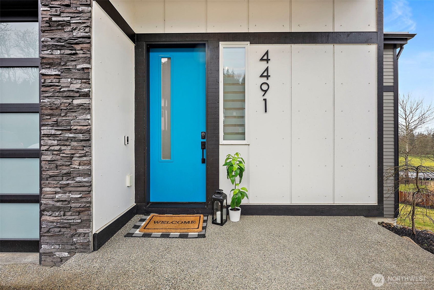 Modern exterior of a contemporary home for sale in the River Rock subdivision, featuring clean architectural lines, stone accents, a spacious driveway, and attached garage. Aerial and front views highlight its setting within the scenic River Rock community surrounded by natural greenery.