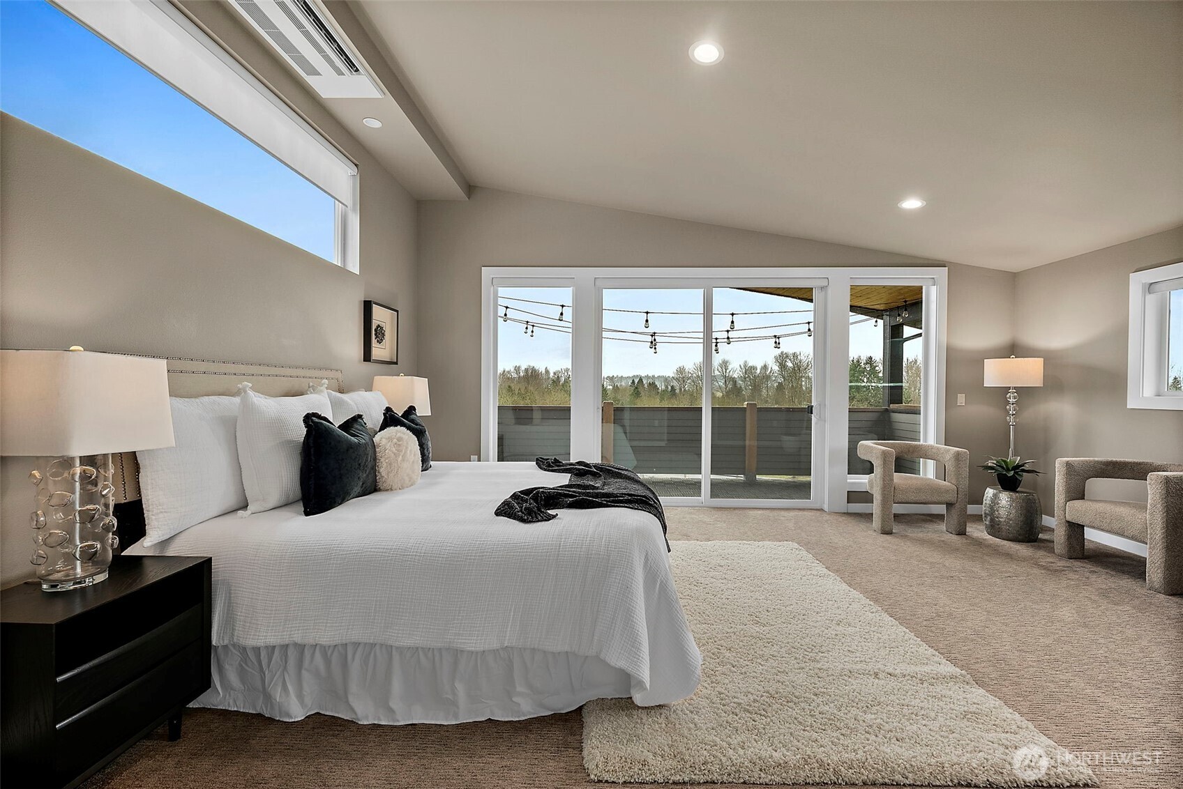 Spacious primary bedroom in this River Rock home in Auburn featuring large windows, soft carpeting, and abundant natural light. The open layout provides a comfortable retreat with plenty of space for a sitting area and relaxing views of the surrounding landscape.