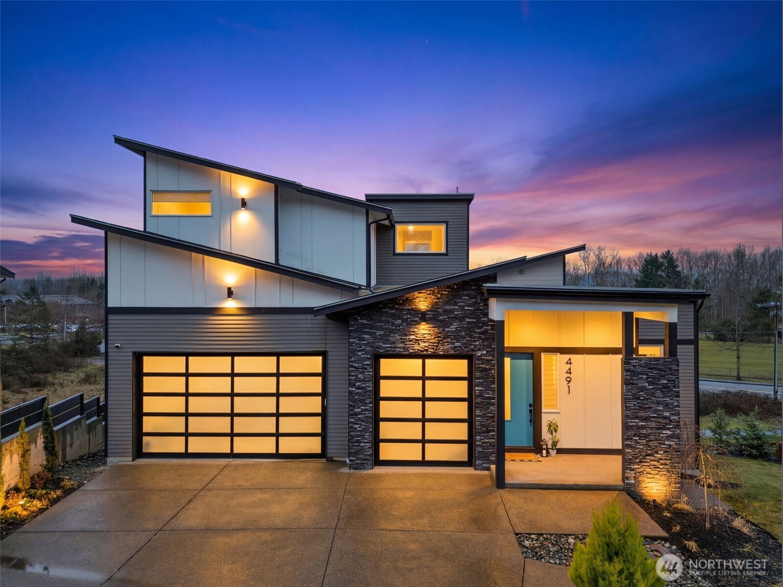 Modern exterior of a contemporary home for sale in the River Rock subdivision, featuring clean architectural lines, stone accents, a spacious driveway, and attached garage. Aerial and front views highlight its setting within the scenic River Rock community surrounded by natural greenery.