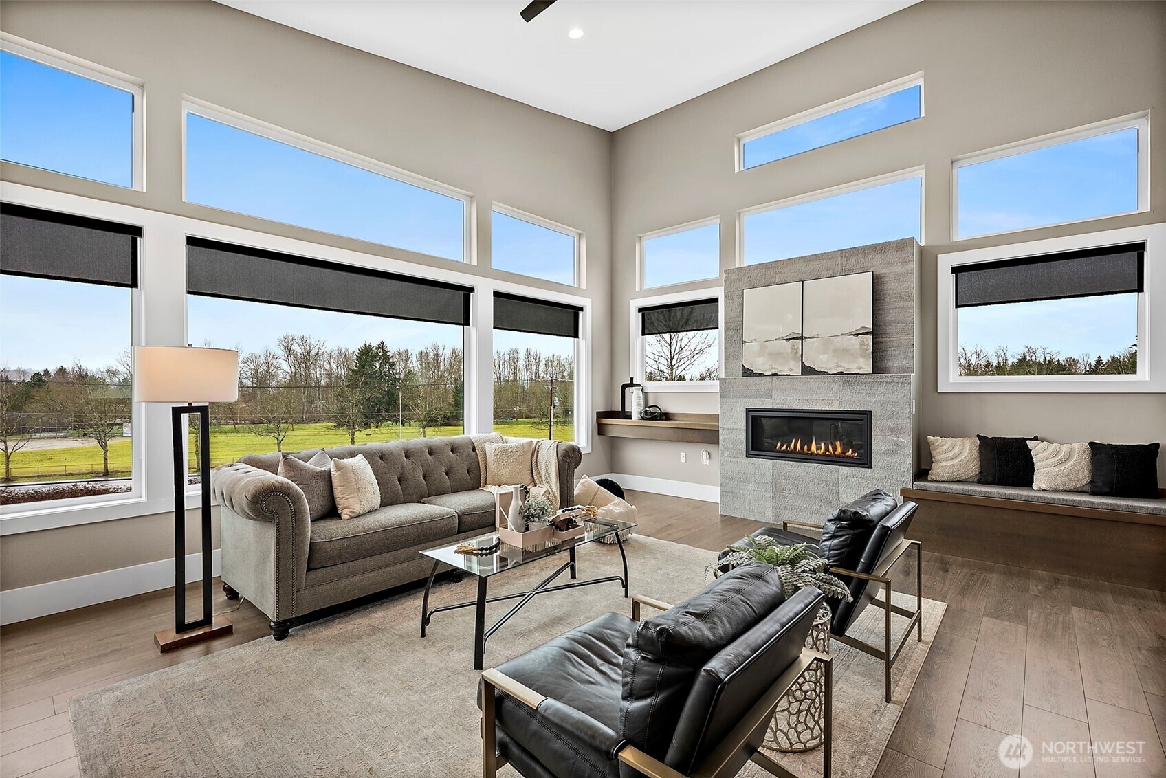 Bright, open living room in a modern home for sale in the River Rock community, featuring floor to ceiling windows, a contemporary fireplace, and abundant natural light. The spacious layout and scenic outdoor views create an inviting space ideal for relaxing or entertaining.
