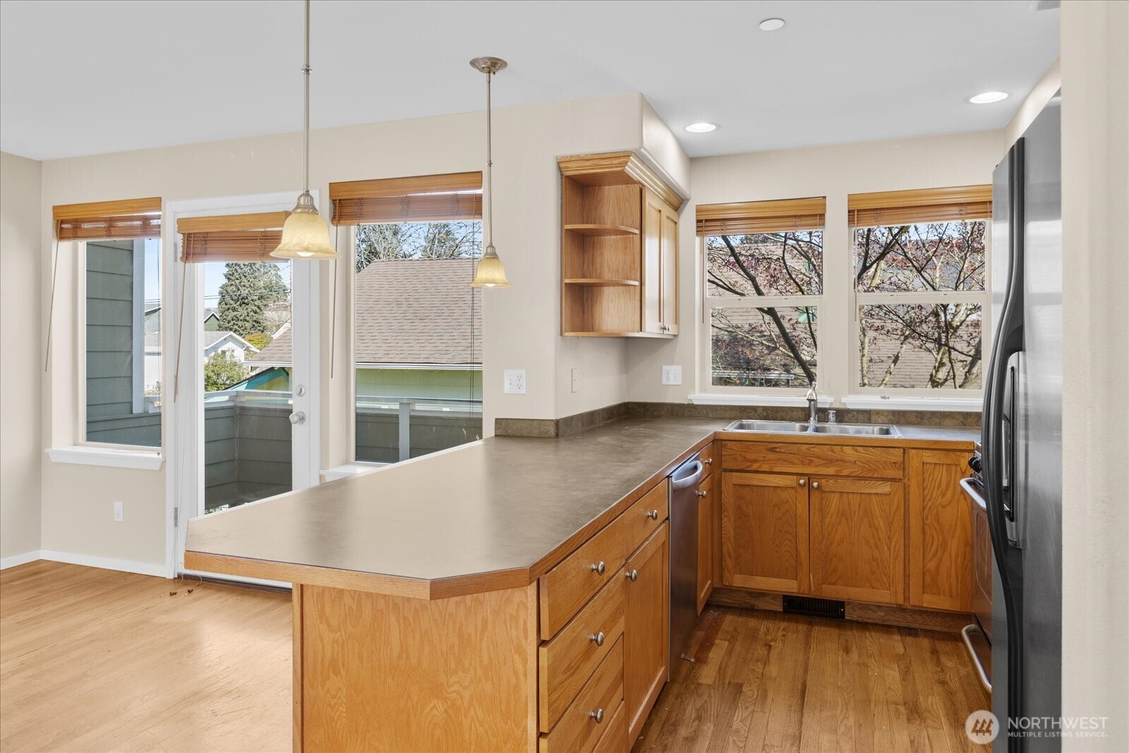 Kitchen with wood cabinetry, stainless steel appliances, pendant lighting, and multiple windows providing natural light.