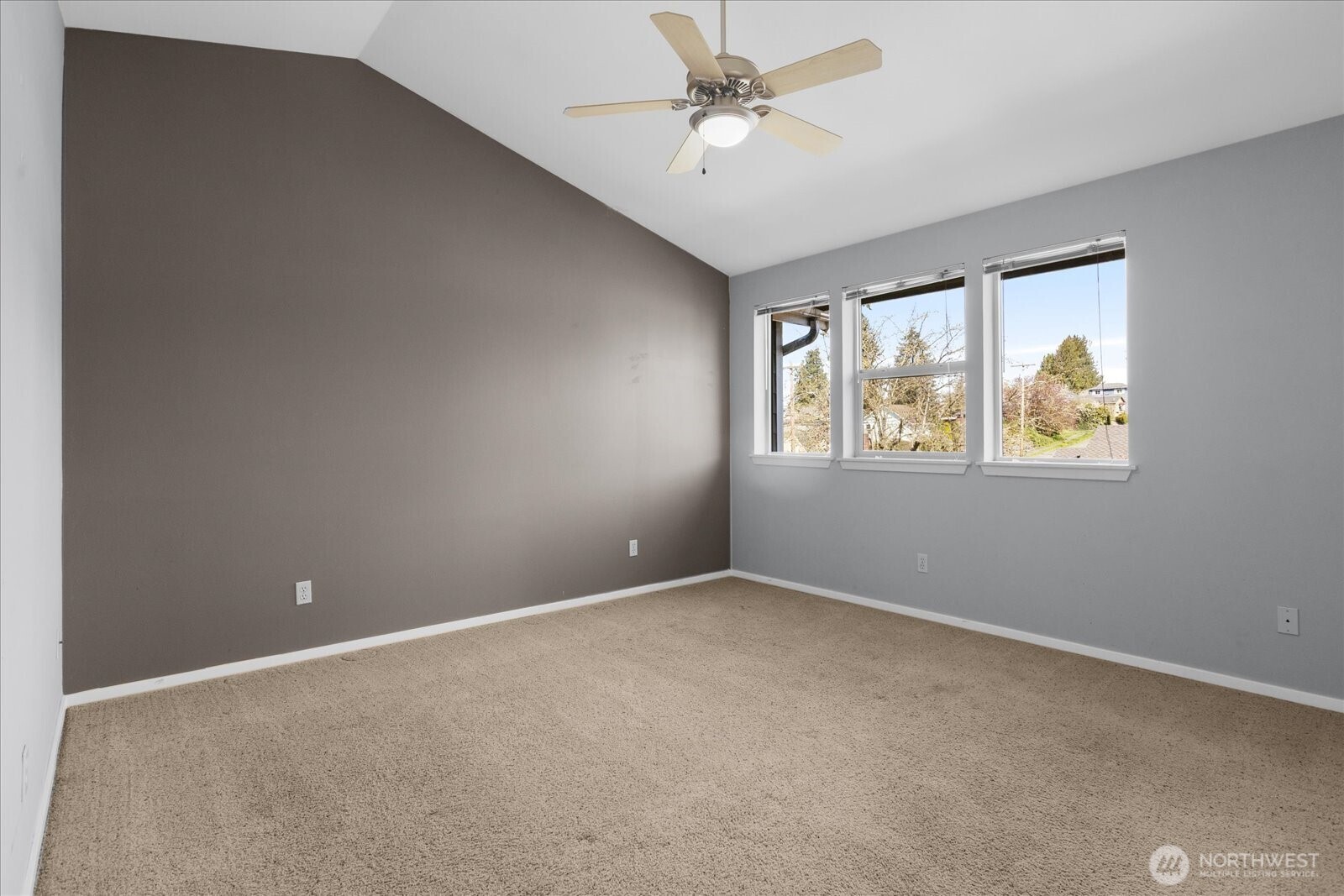 Primary bedroom with vaulted ceiling, ceiling fan, carpeted flooring, and windows.