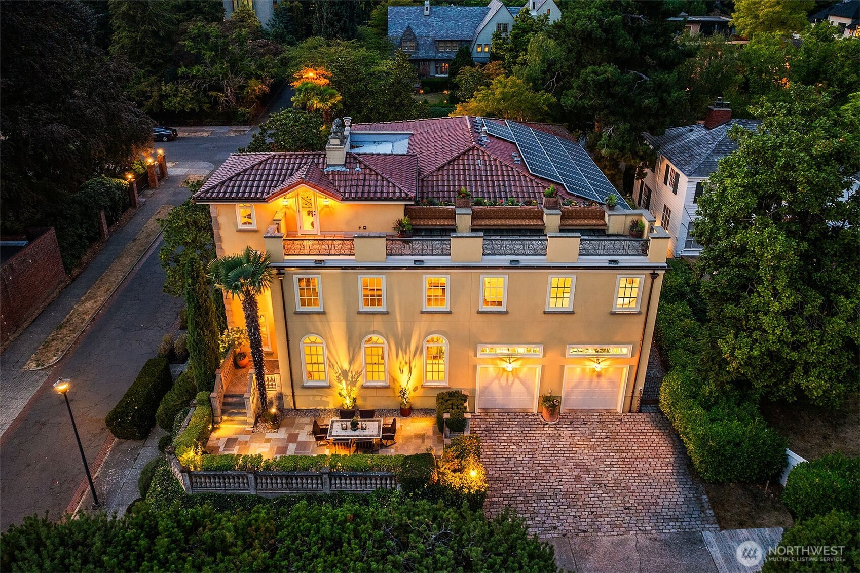 Aerial view of home's south exterior featuring terraced back patio, rooftop view deck, and tile roof with 9.4 kW solar array providing renewable power to the property.