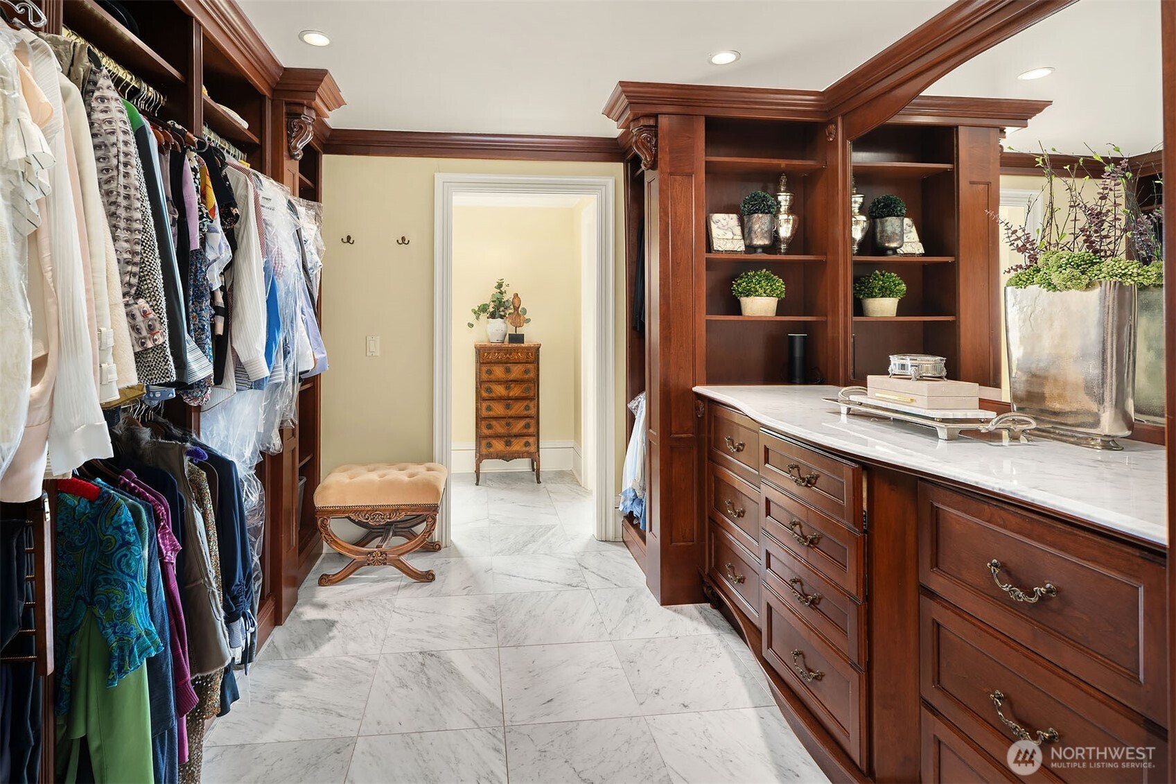 Primary walk-in closet with fine, custom built-in organizers and dresser with Carrara marble countertop and mirror.