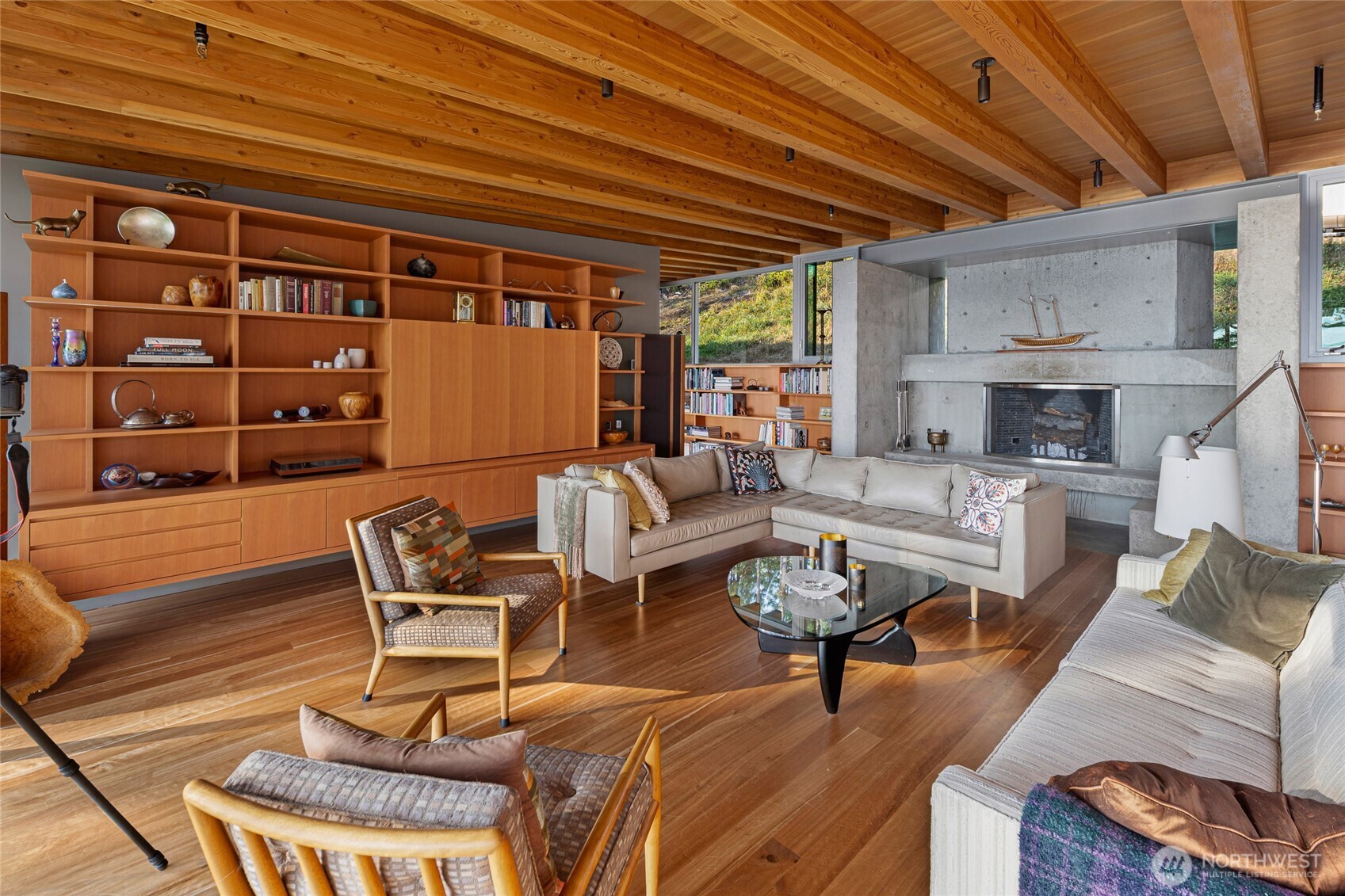 The sophisticated great room showcases exposed timber beams, custom built-ins, and a sculptural concrete fireplace, creating a warm yet modern gathering space designed to frame the surrounding San Juan Island natural landscape.