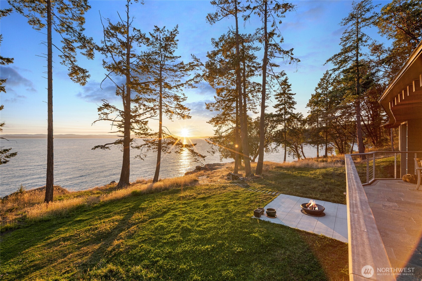 Golden sunset light pours across the property, illuminating the lawn and patio while the horizon stretches across Haro Strait toward the Olympic Mountains—a signature experience of San Juan Island west side living.