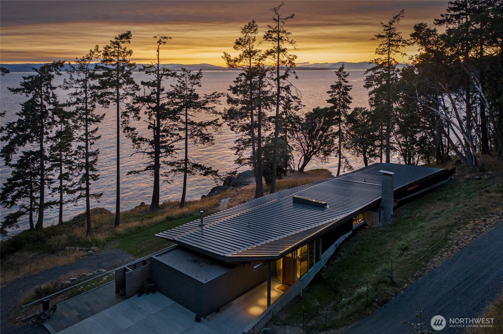 Golden hour on the west side of San Juan Island, where the home’s long, modern roofline frames breathtaking sunset views over Haro Strait—one of the most sought-after vantage points in the San Juan Islands.