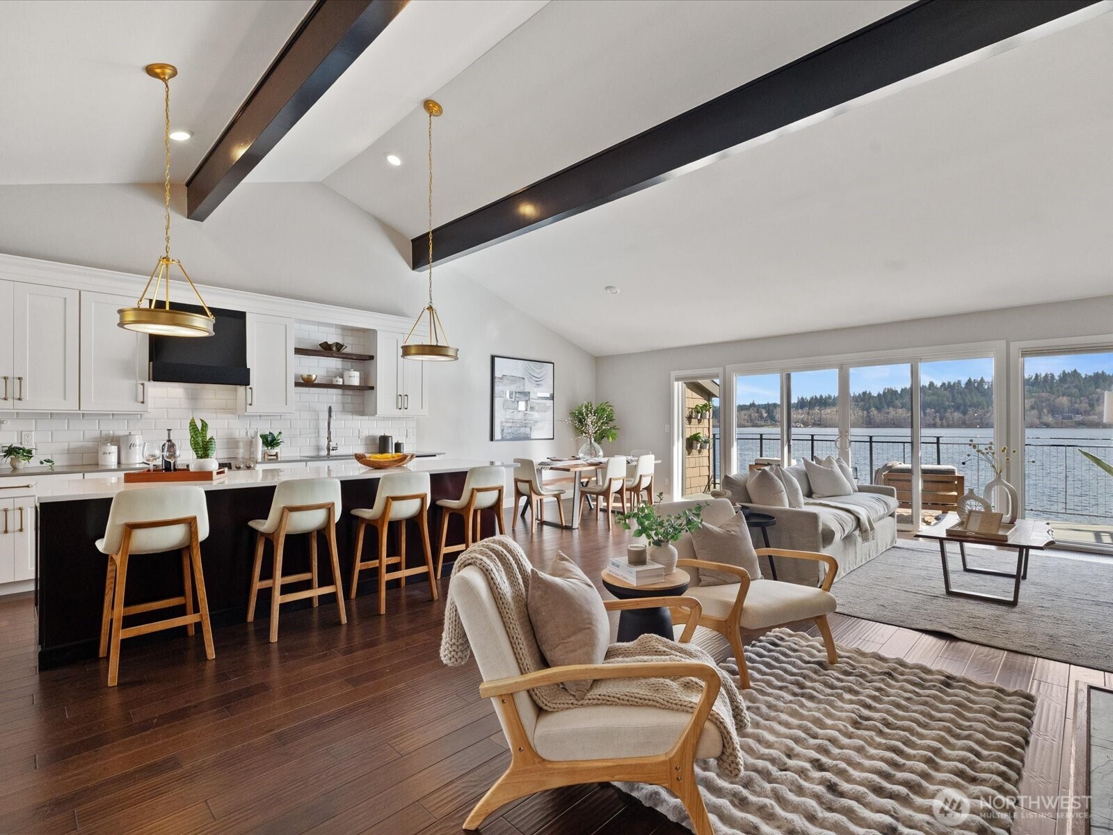 Open-concept living and kitchen area with island seating, vaulted ceilings, hardwood flooring, and access to waterfront deck