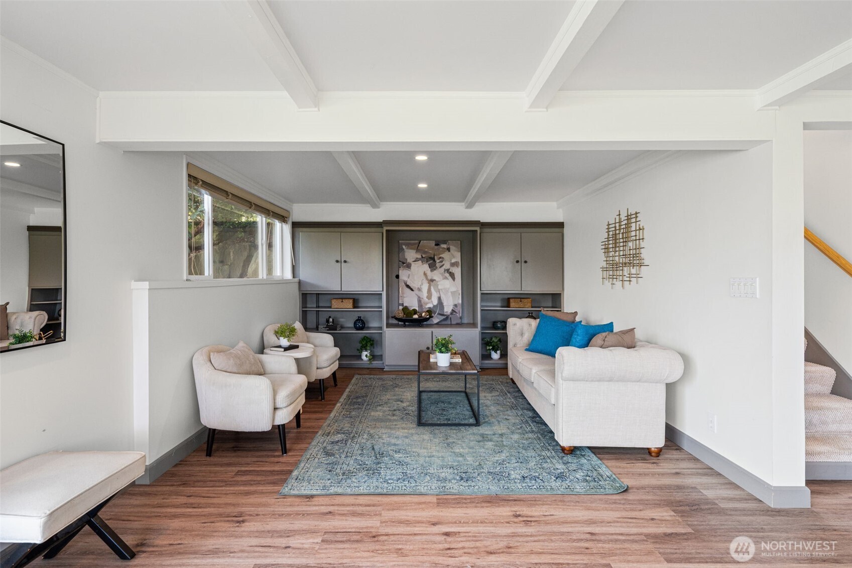 Versatile living area with built-in shelving and ample room for seating, media, or play. Clean lines, beam accents, and recessed lighting enhance the space, while a hidden storage area tucked behind the cabinetry adds extra functionality.