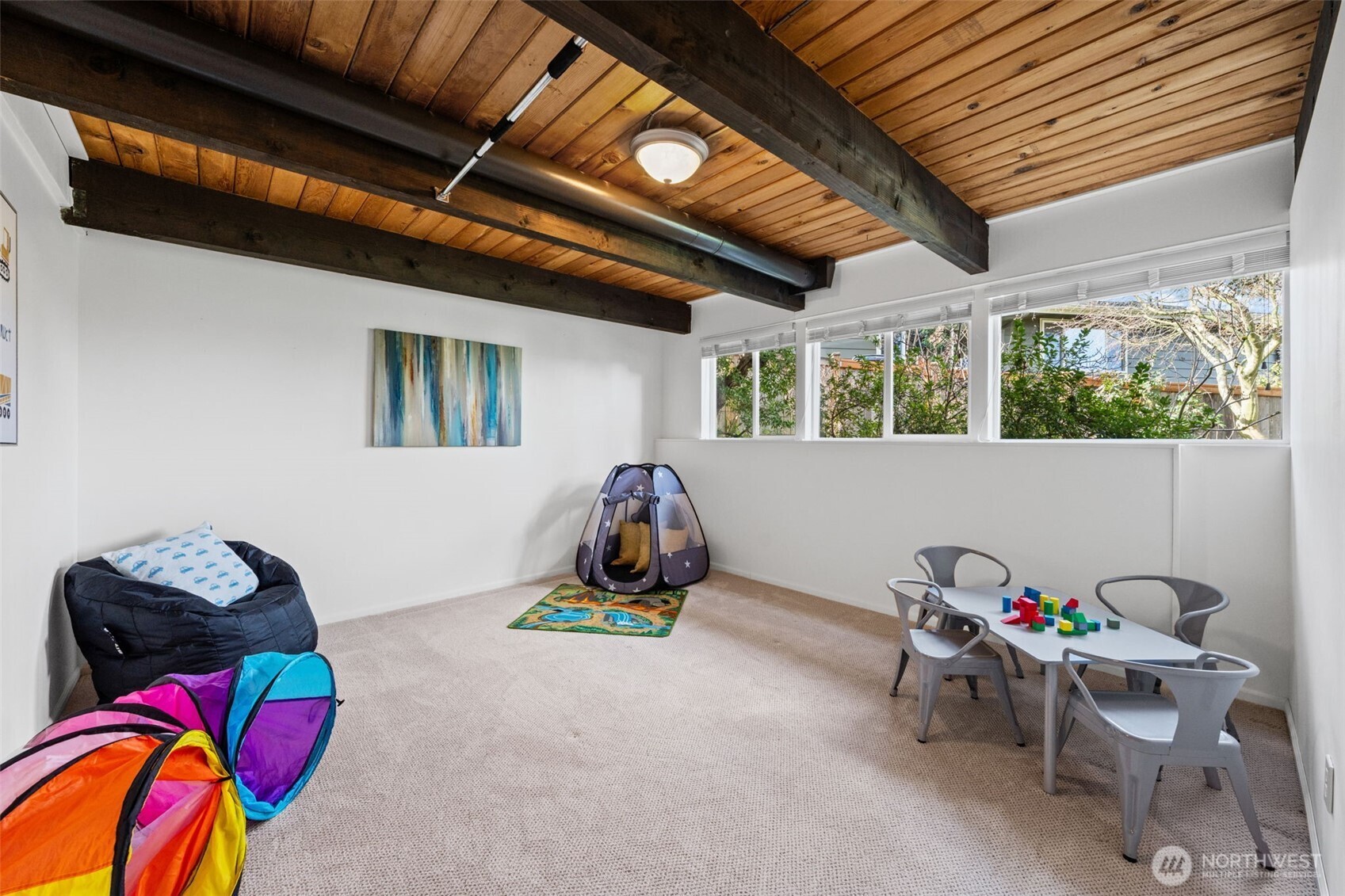 Lower-Level Bedroom Four features wide windows bringing in soft natural light. Exposed wood beam ceiling adds character, while the flexible layout supports a bedroom, playroom, or additional living space.