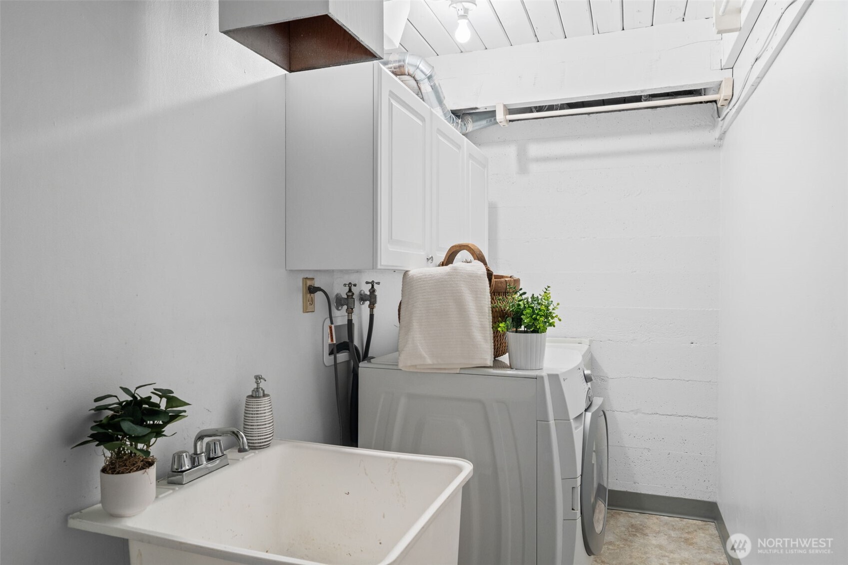 Functional lower-level utility space with washer and dryer, utility sink, and overhead storage. Practical layout offers room for laundry tasks, storage, and household organization.