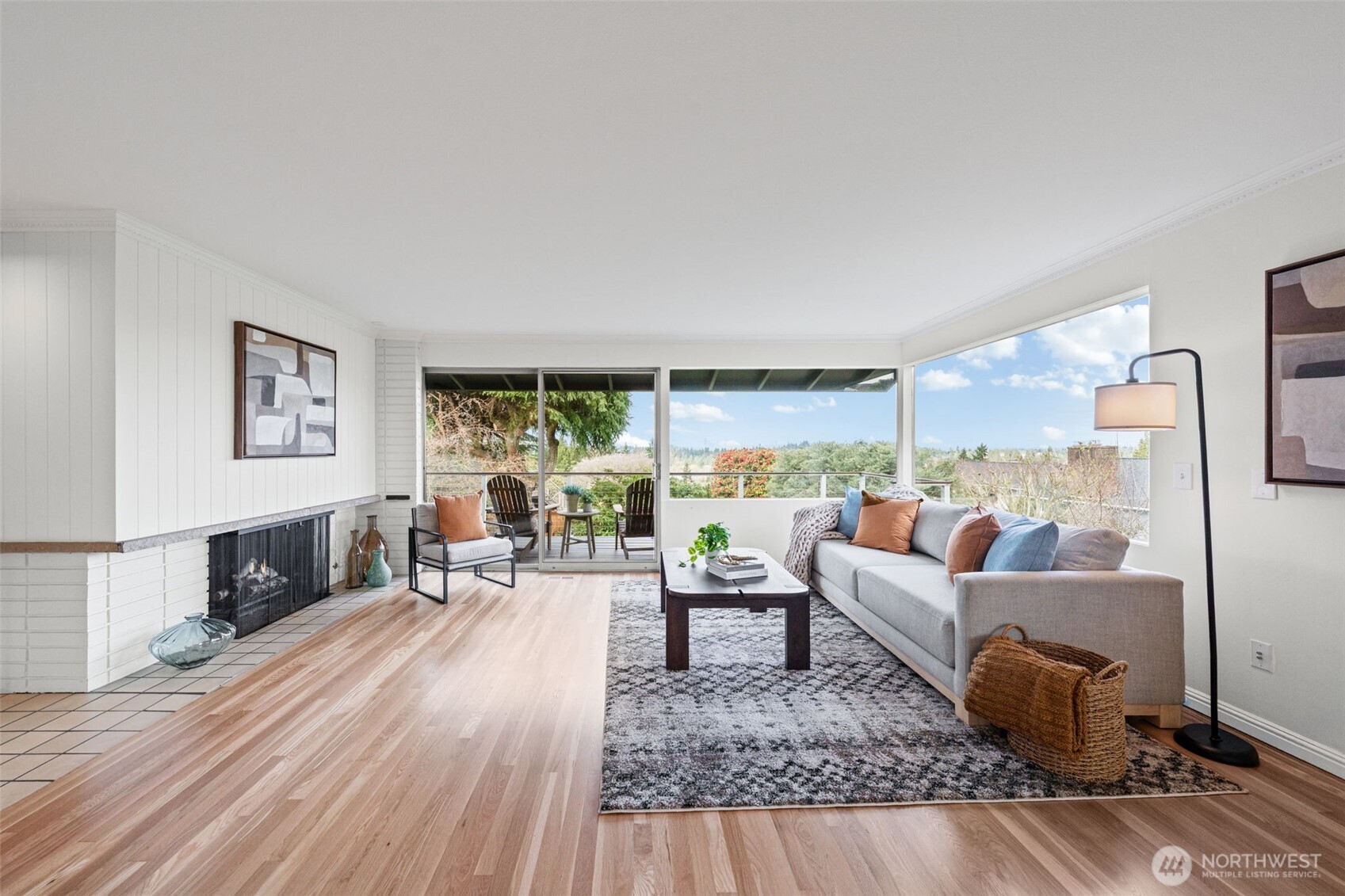 Light-filled living room with expansive windows and seamless indoor-outdoor flow to a private deck with territorial views. Warm hardwood floors and a cozy fireplace create an inviting space for everyday living and entertaining.