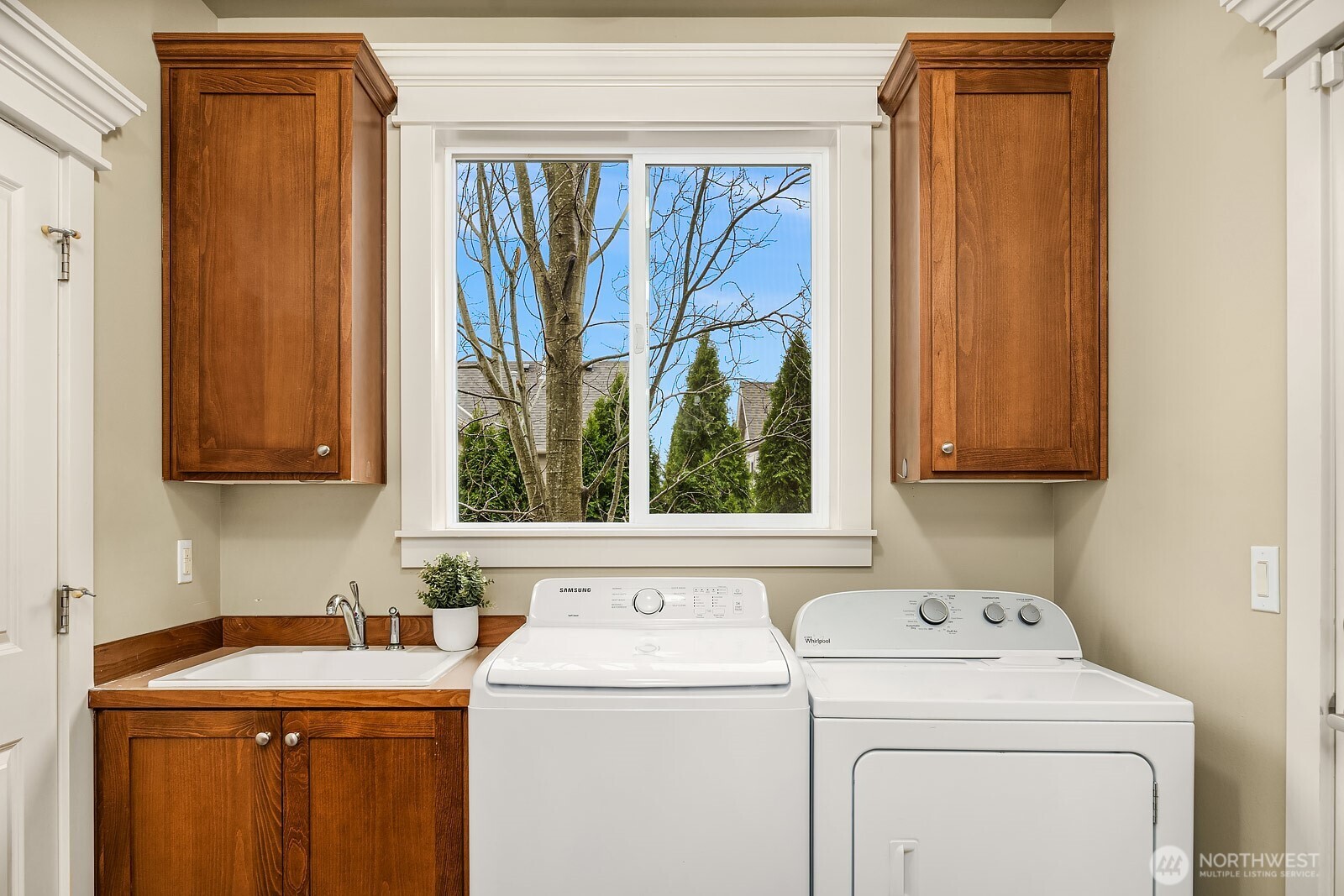 The conveniently located laundry room features a full-size washer and dryer, warm wood cabinetry for ample storage, and a utility sink — a well-appointed and practical space that makes everyday chores a breeze.