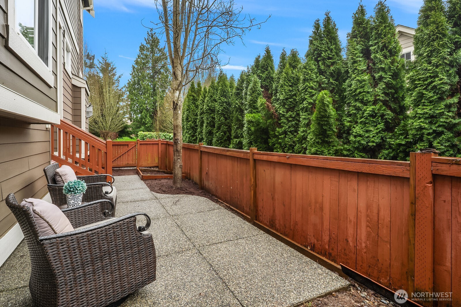 Another view of the private patio showcases the fully fenced yard and lush evergreen backdrop — a serene and secluded outdoor space perfect for entertaining, relaxing, or simply enjoying the natural beauty of the surrounding landscape.