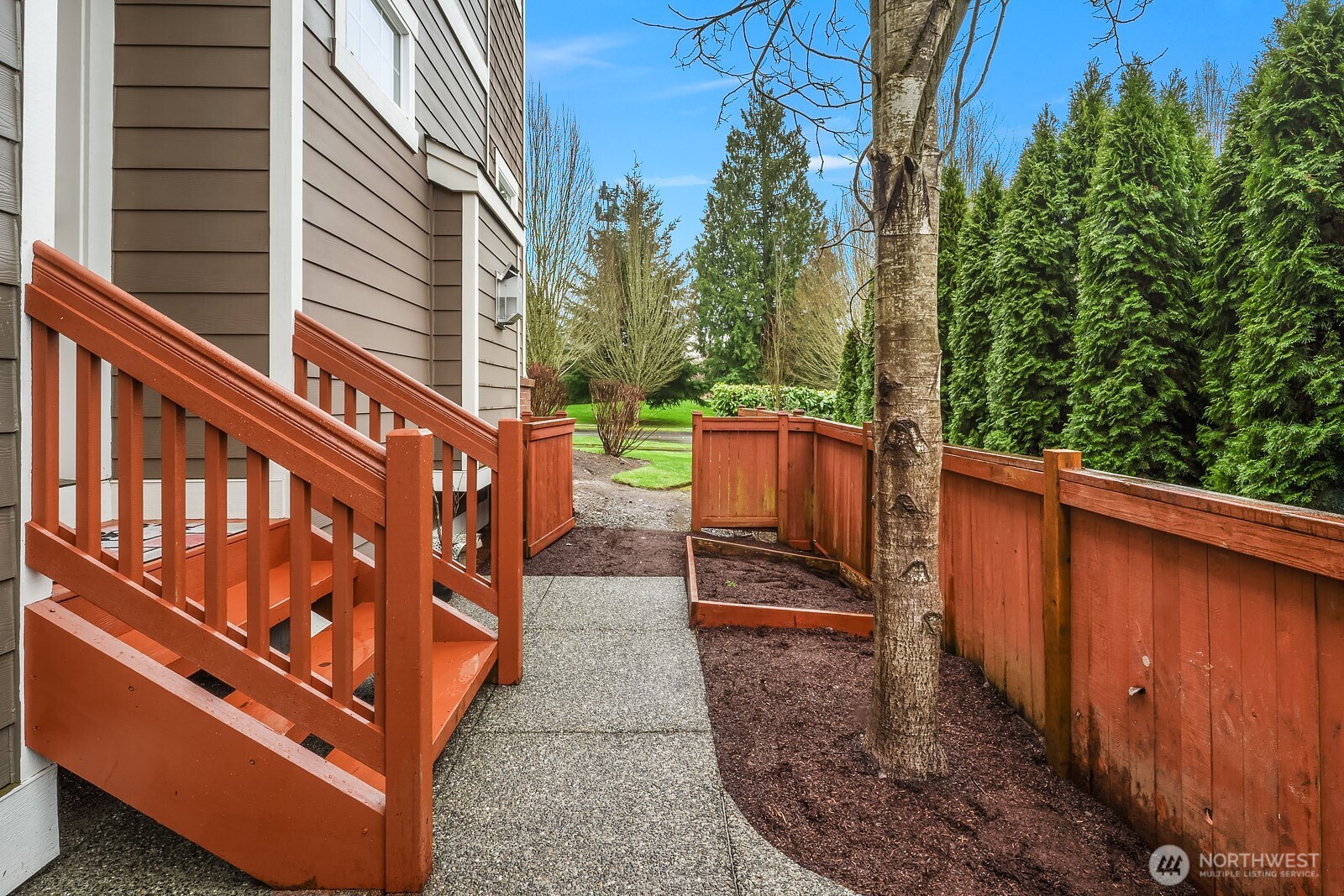 The home's exterior walkway and staircase highlight the corner lot setting, with mature evergreen trees providing a beautiful natural backdrop and a separate entrance that leads conveniently to the above-garage ADU.