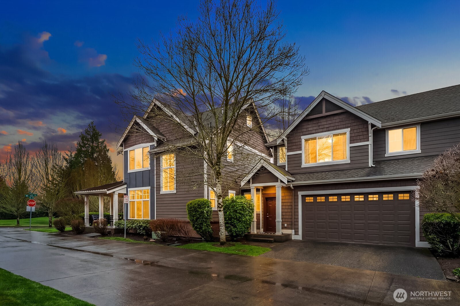 Another stunning evening exterior shot highlights the home's impressive presence on the corner lot, with the warm glow of interior lights, classic Craftsman detailing, and a spacious three-car garage creating an unforgettable first impression.