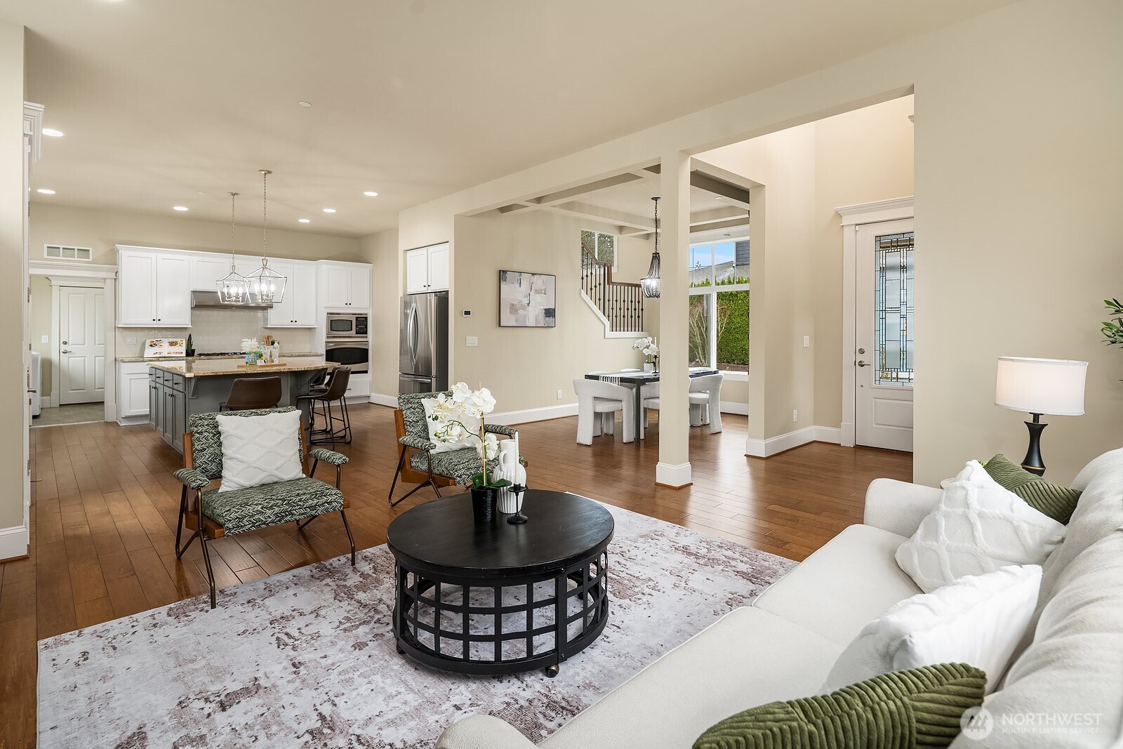 This view showcases the seamless flow between the living room and the expansive kitchen beyond, highlighting the home's open and connected layout with rich engineered hardwood floors anchoring the entire main level.