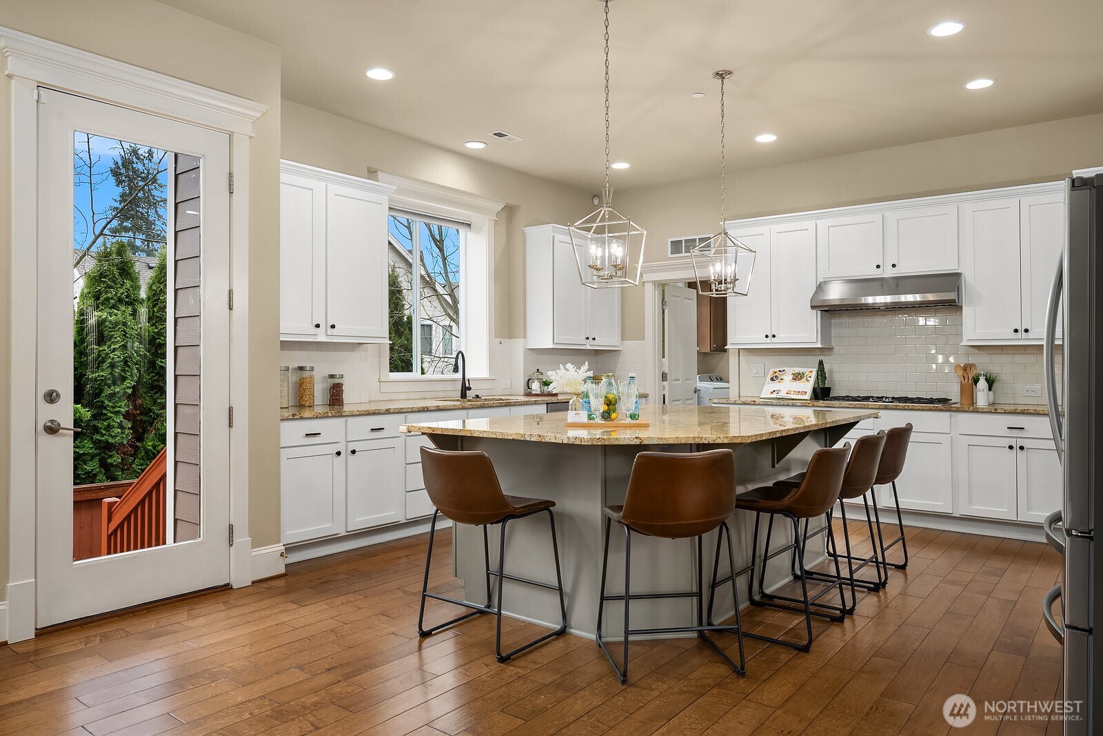The expansive kitchen is a chef's dream, featuring a wraparound island with seating, premium appliances, crisp white cabinetry, and abundant storage — all bathed in natural light for a bright and highly functional workspace.