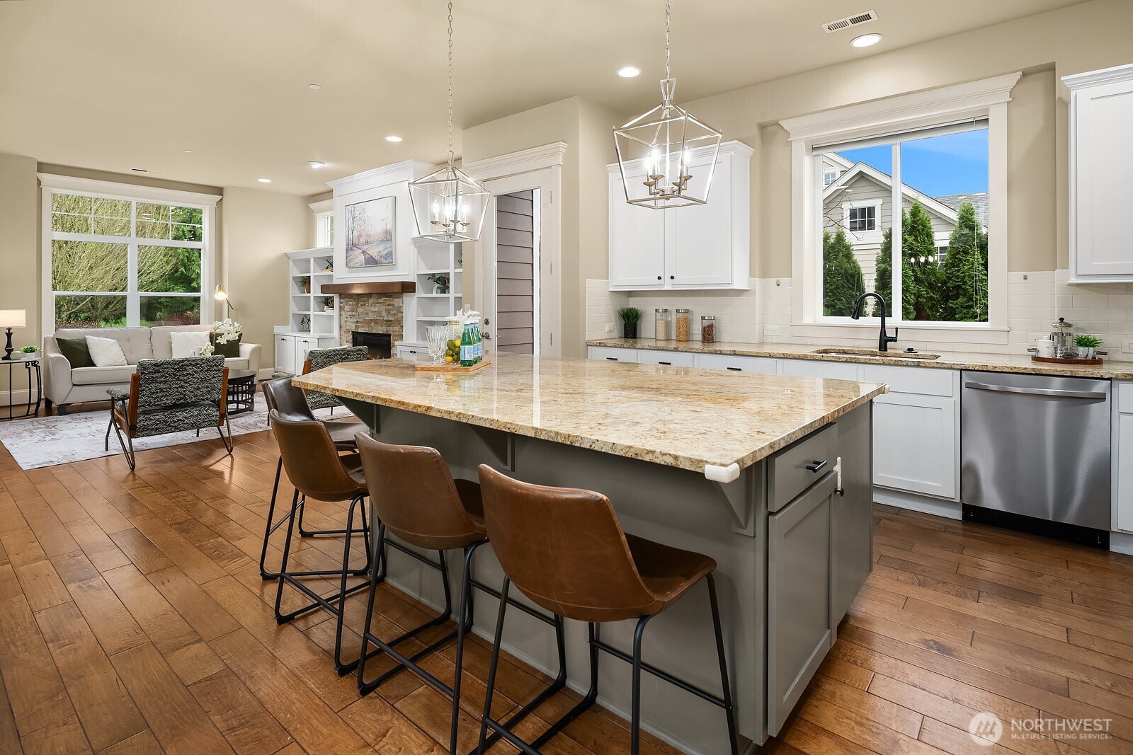 This sweeping view of the kitchen and living areas captures the home's seamless open-concept flow, with the large island, warm hardwood floors, and abundant natural light creating an inviting and cohesive space perfect for gathering.